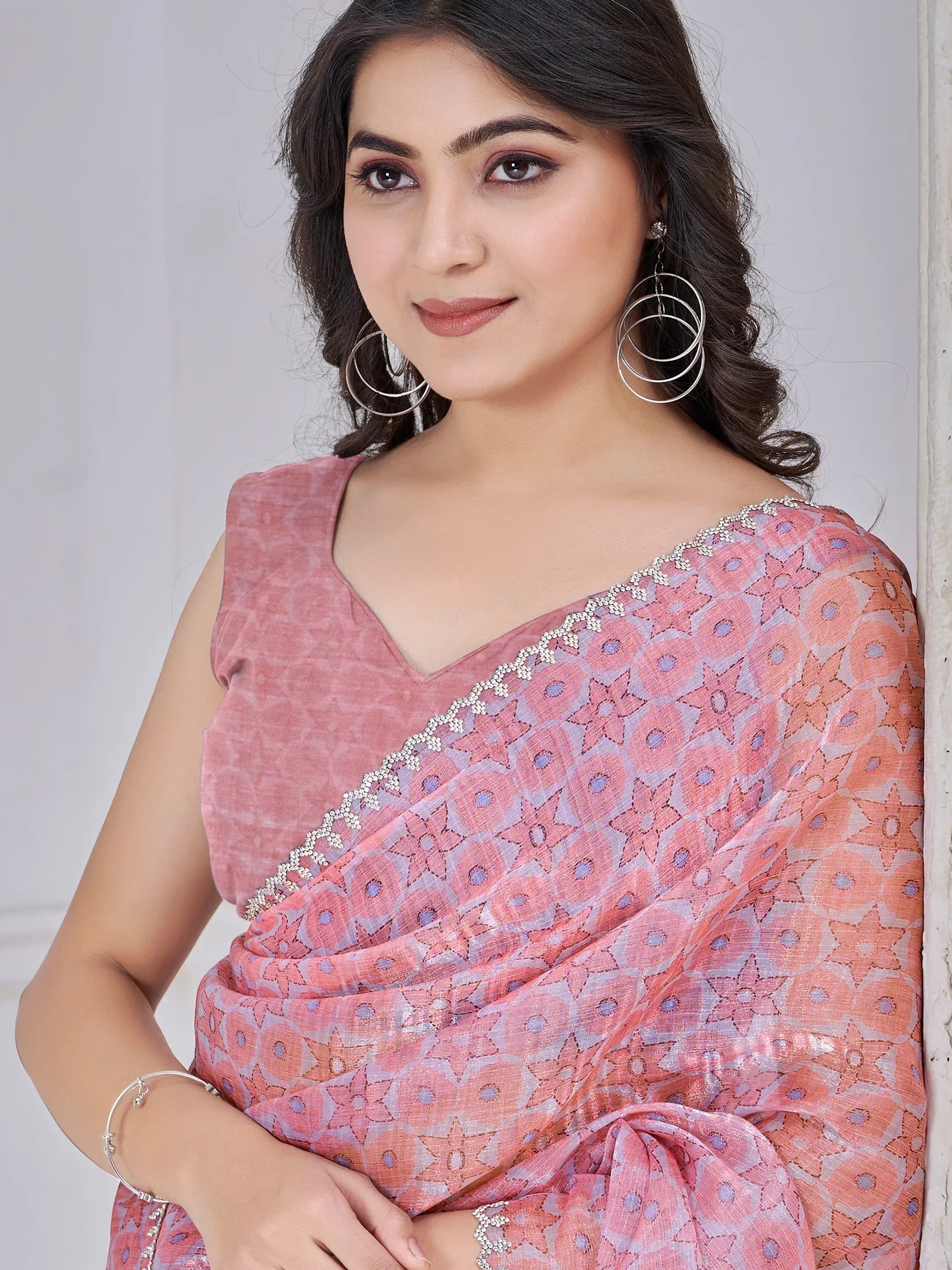 Pink floral printed saree with embellished border and matching blouse, styled with statement earrings