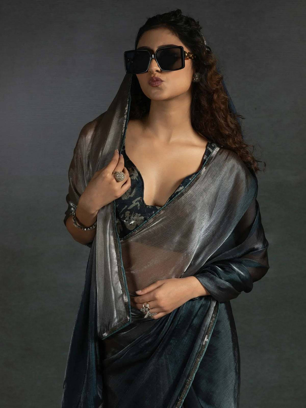 Stylish woman in dark blue velvet saree with sheer dupatta, statement sunglasses, and ethnic jewelry