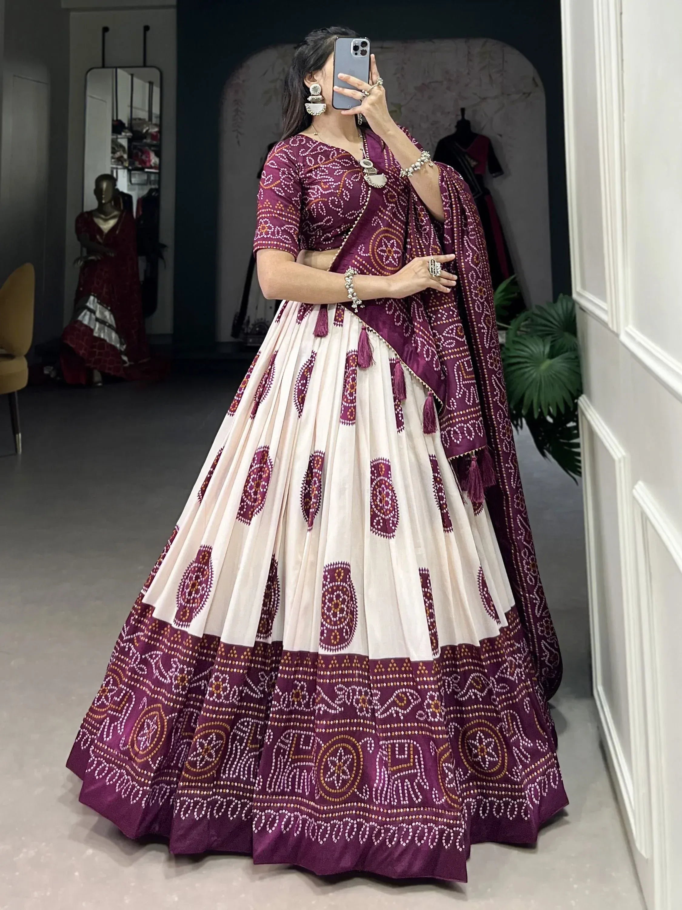 Woman in maroon and cream printed lehenga choli with mirror work, taking mirror selfie in boutique