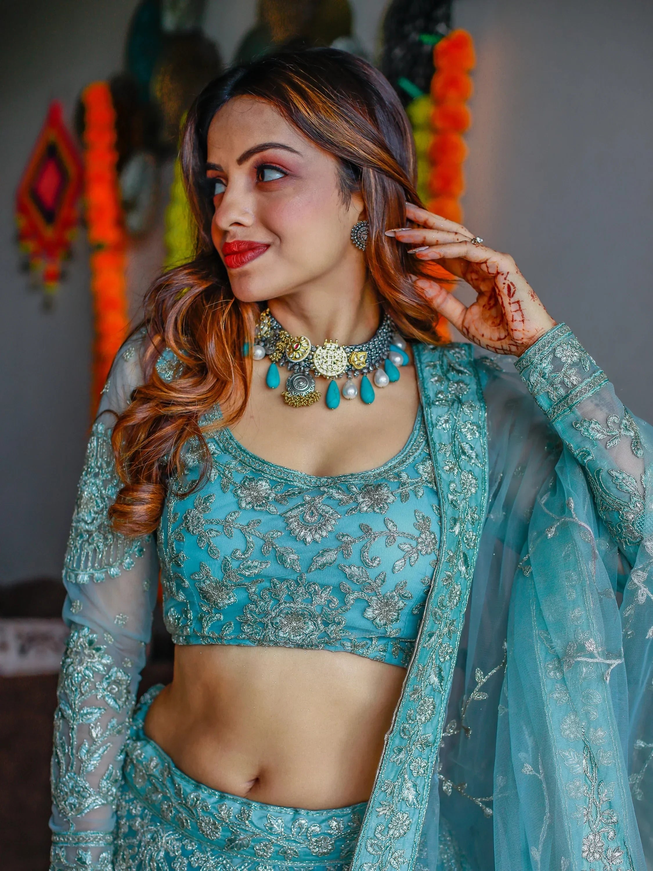Teal embroidered lehenga choli with silver floral work, sheer sleeves, and statement jewelry for Indian ethnic wear