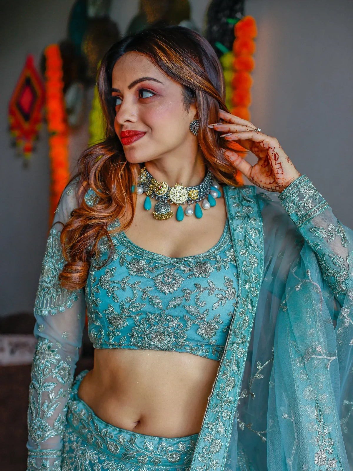Teal embroidered lehenga choli with silver floral work, sheer sleeves, and statement jewelry for Indian ethnic wear