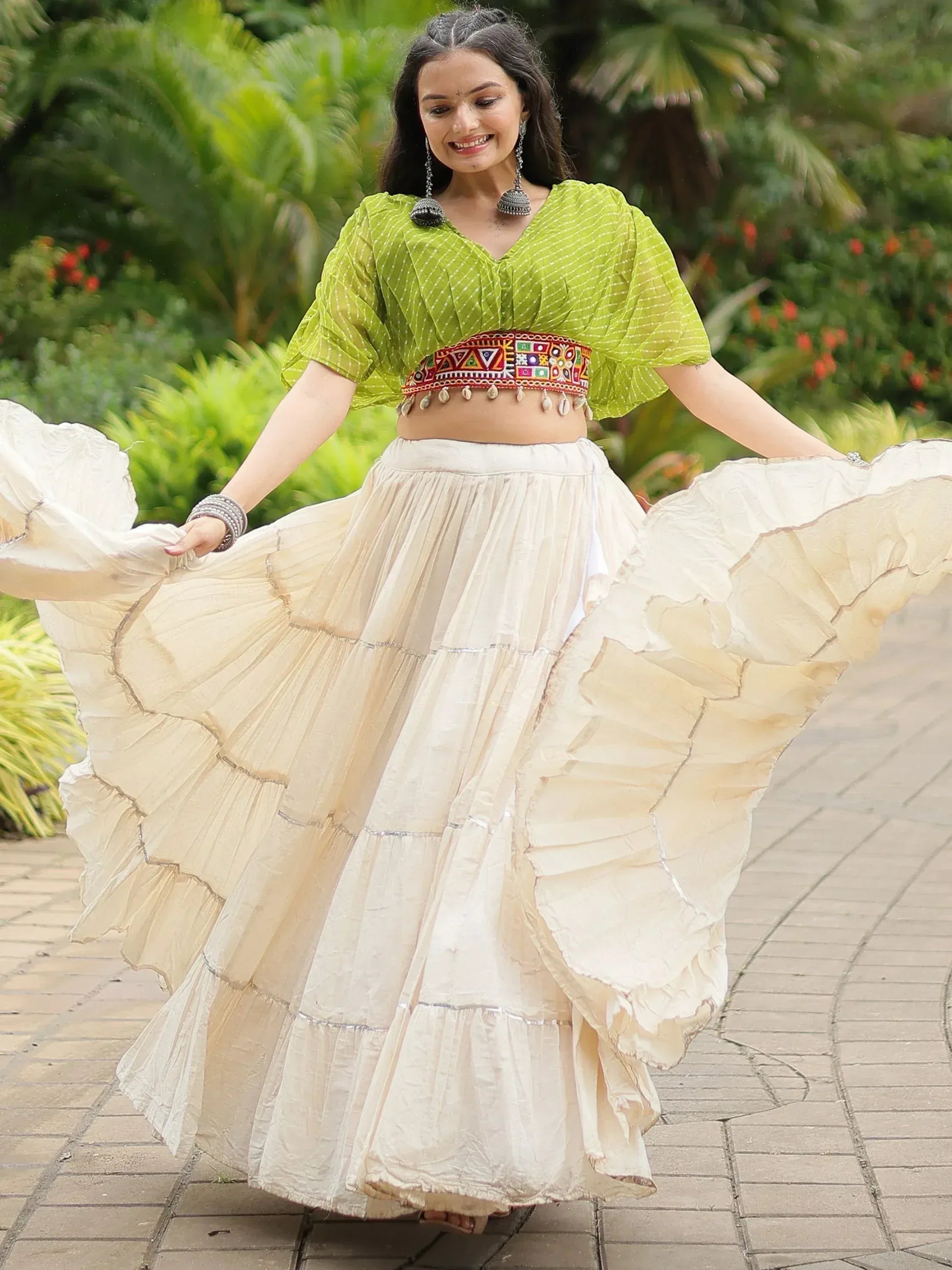 Woman in green printed top and cream ruffled skirt, twirling outdoors, ethnic wear outfit
