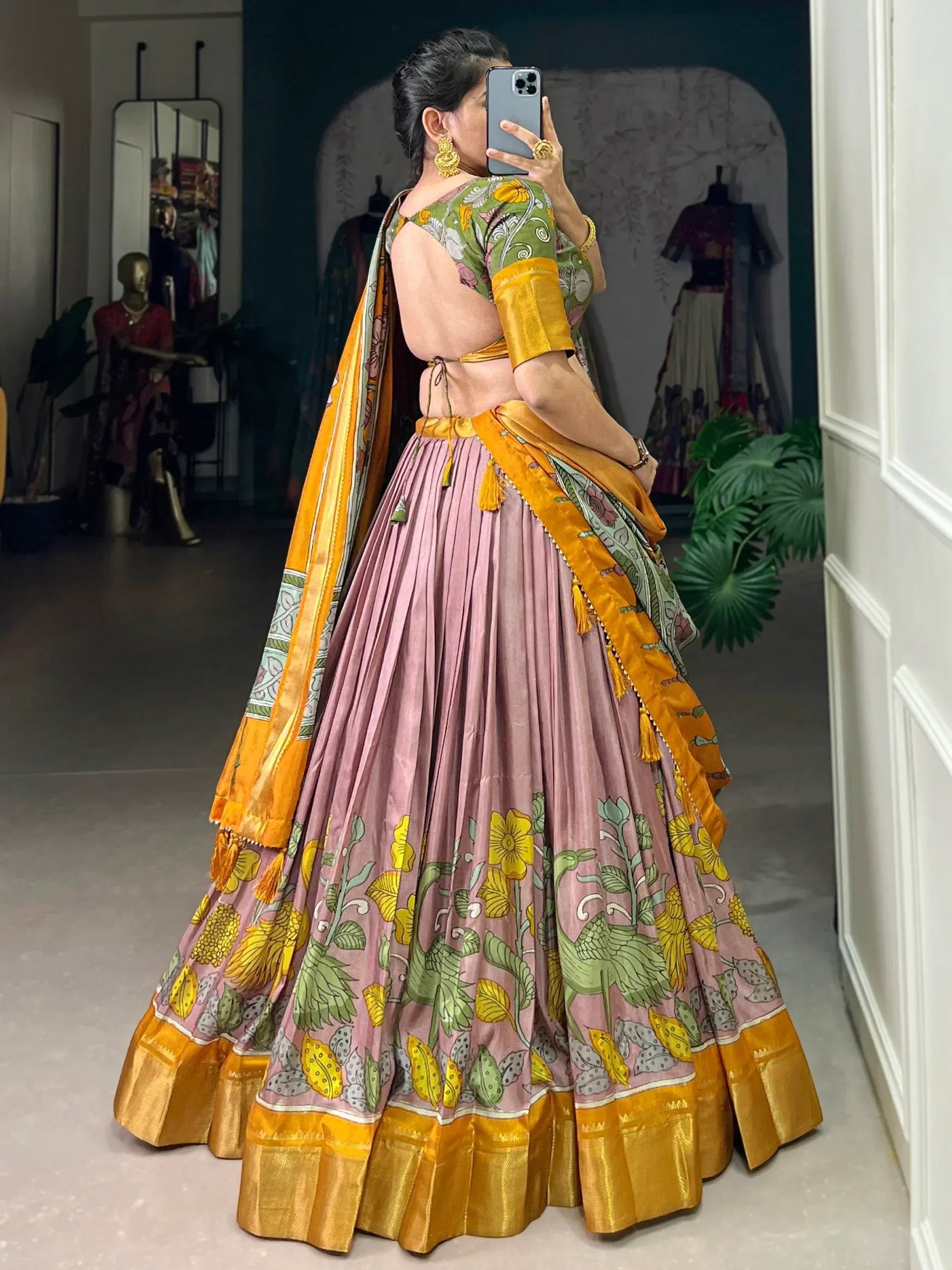 Woman in floral print lehenga choli with pink skirt, green blouse, and yellow dupatta, taking mirror selfie