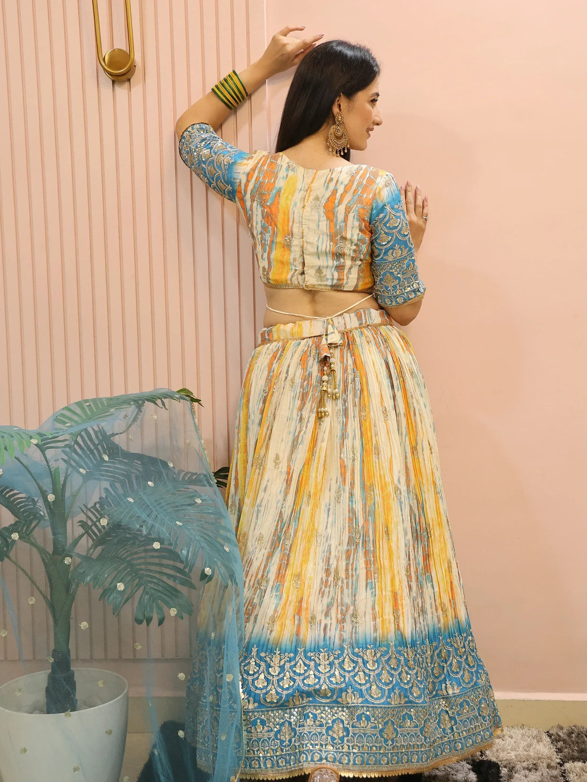 Woman in colorful printed lehenga choli with blue embroidery, gold jewelry, and sheer dupatta, perfect for Indian ethnic occasions.