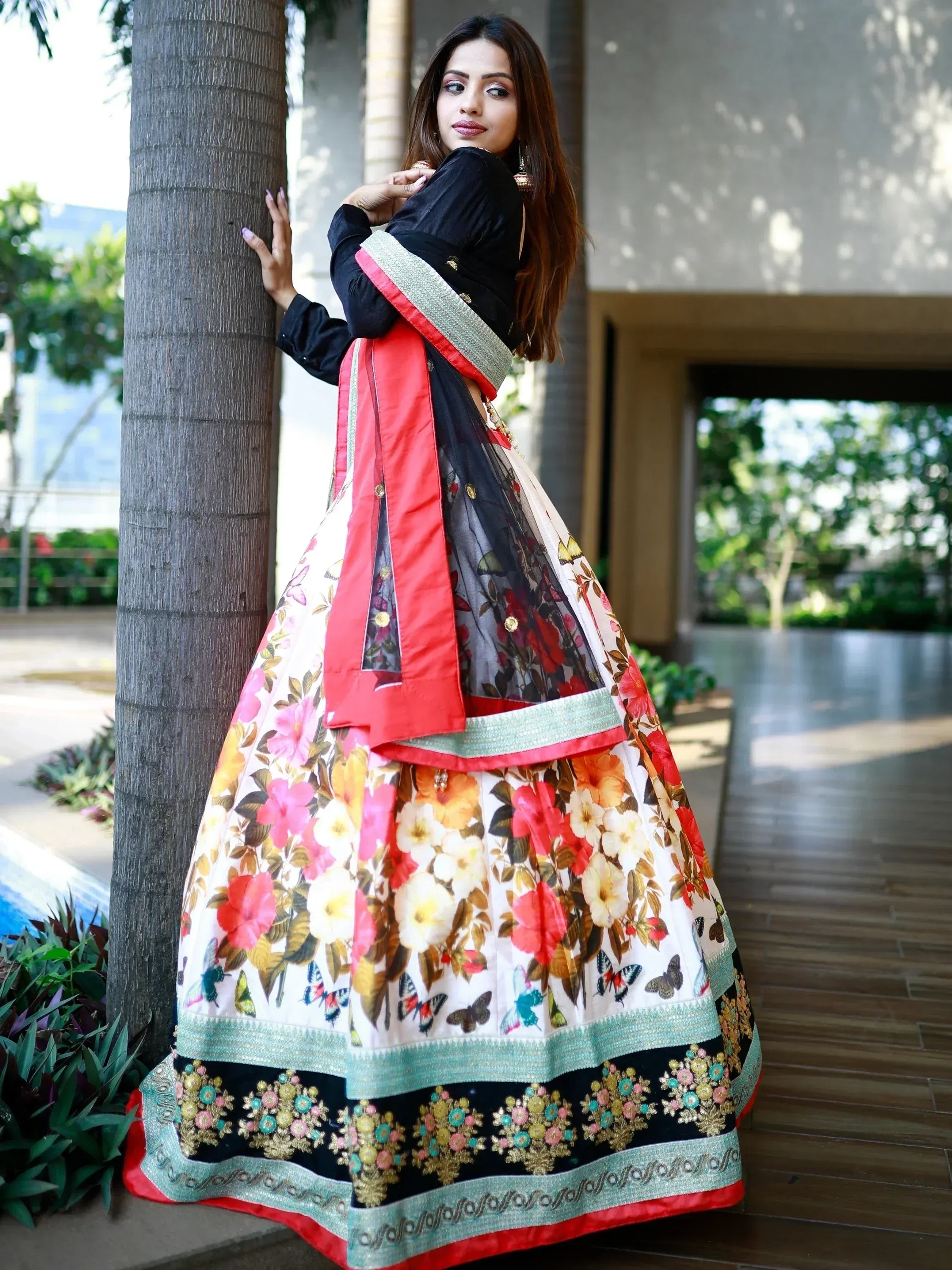 Woman in floral print lehenga choli with black blouse and embroidered border, standing by palm tree