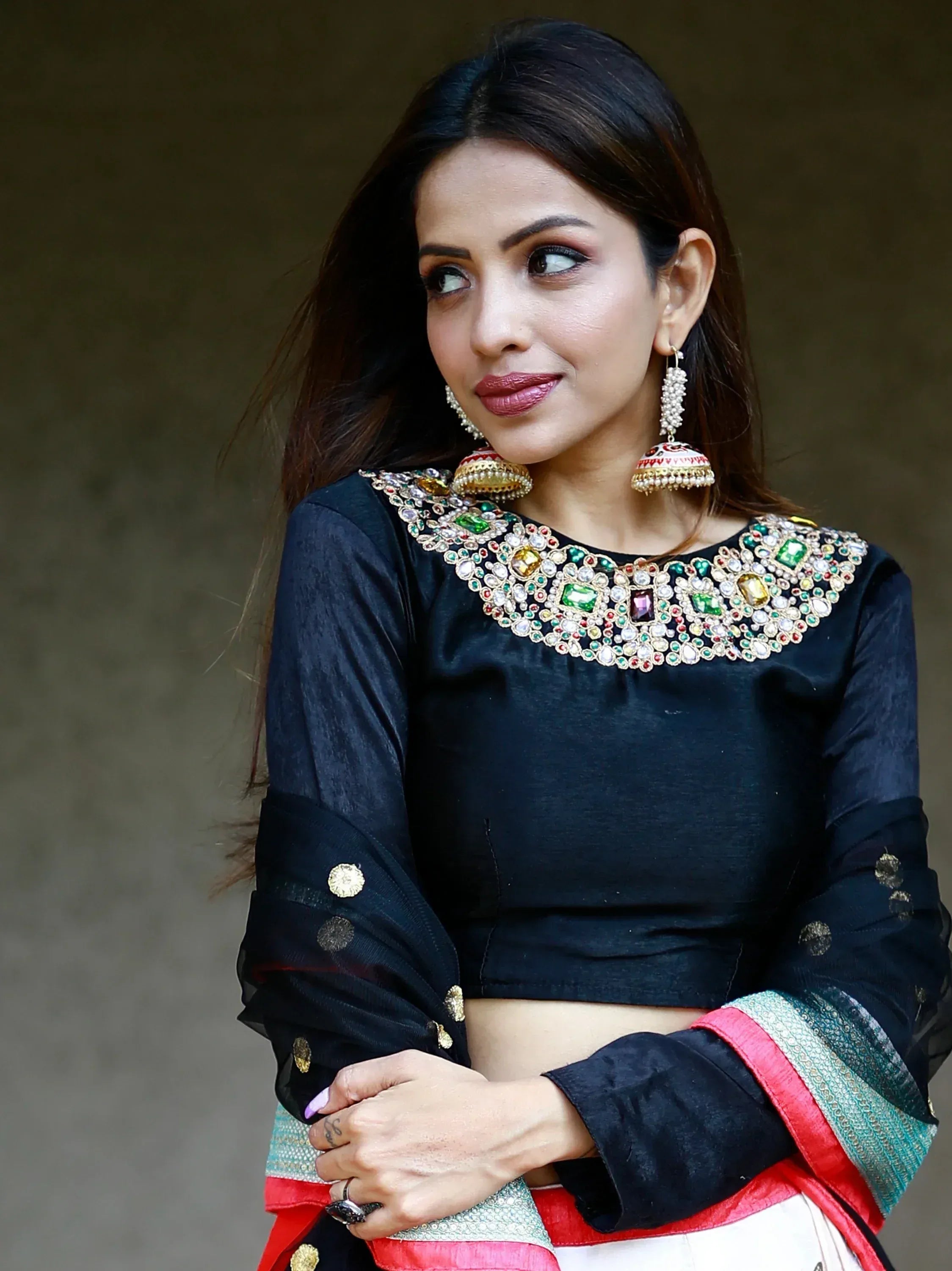 Woman in black embroidered ethnic top with colorful gemstone neckline and jhumka earrings