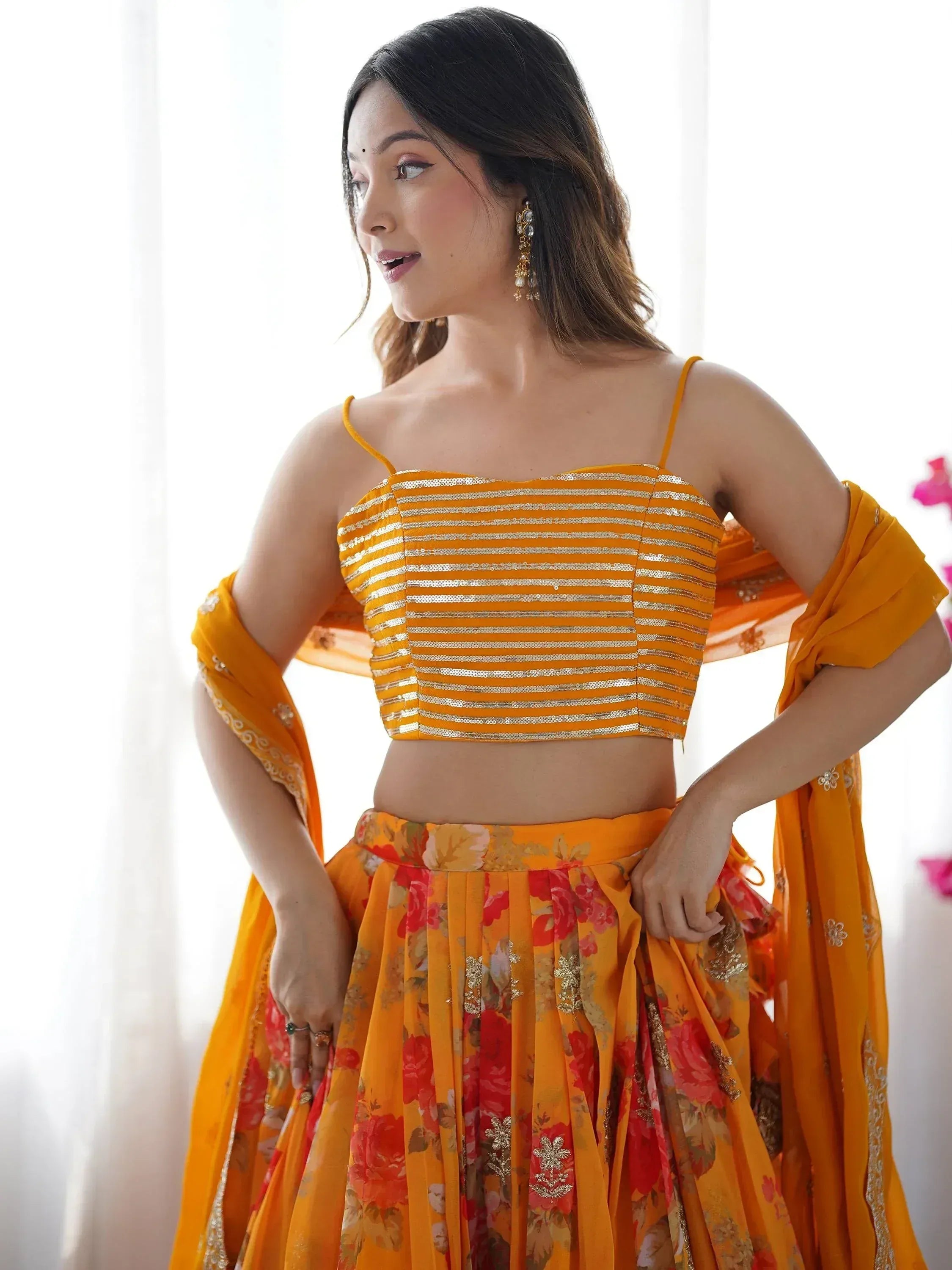 Woman in vibrant orange lehenga choli with floral print and sequin top, perfect for Indian ethnic occasions.