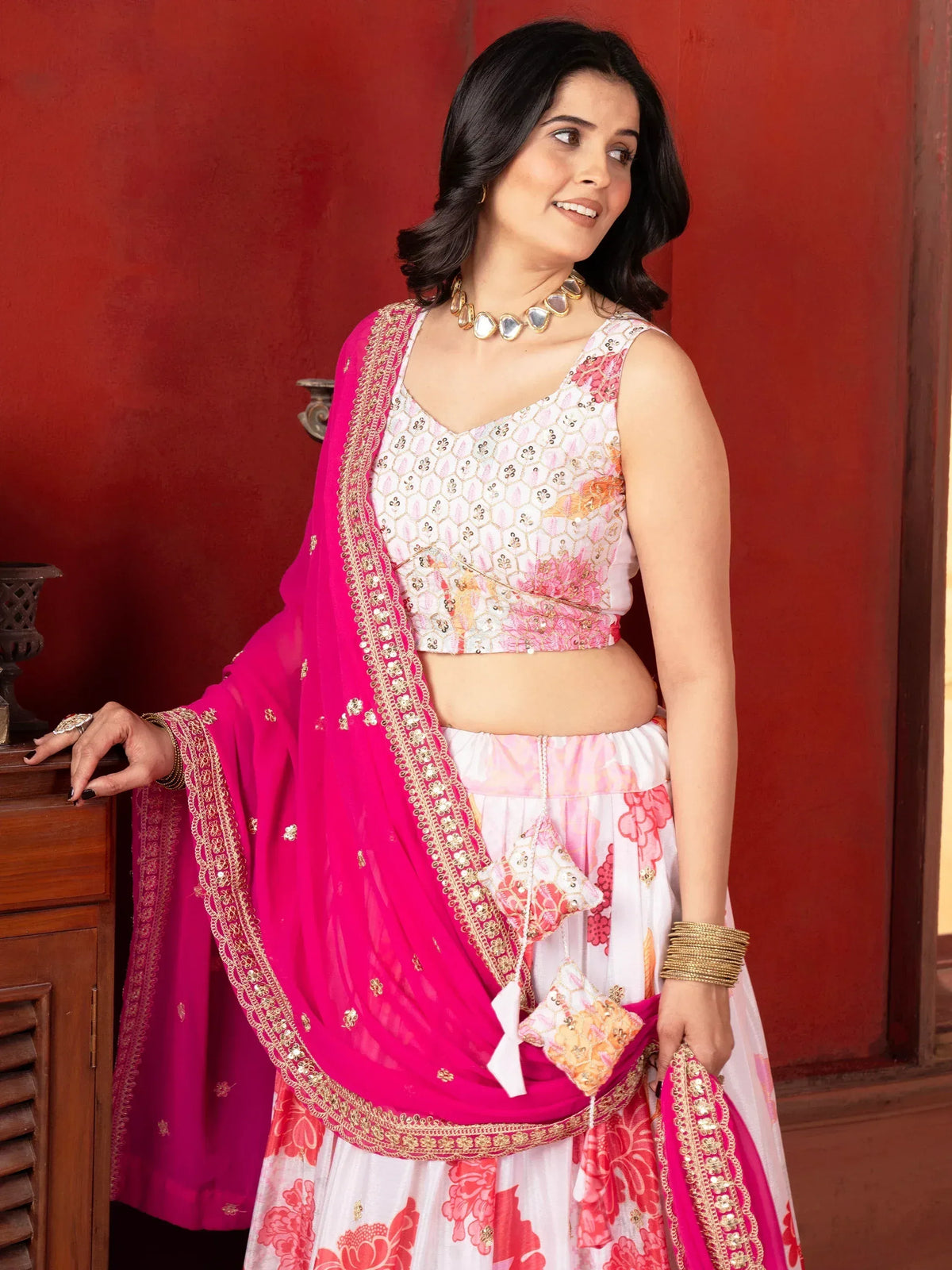 Woman in floral print lehenga choli with pink dupatta, gold embroidery, and traditional jewelry