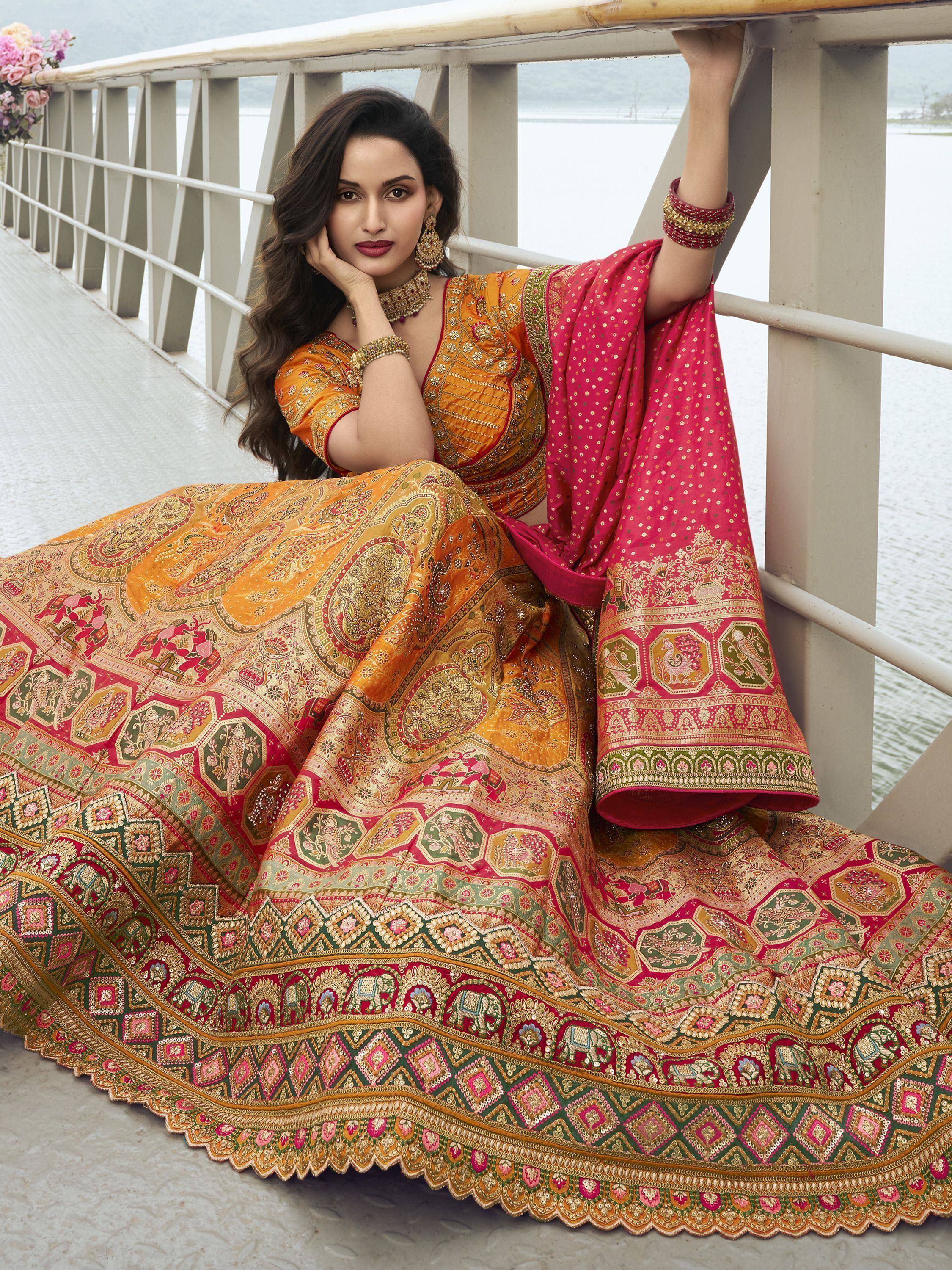 Woman in vibrant orange and pink embroidered lehenga choli, posing on bridge with lake view