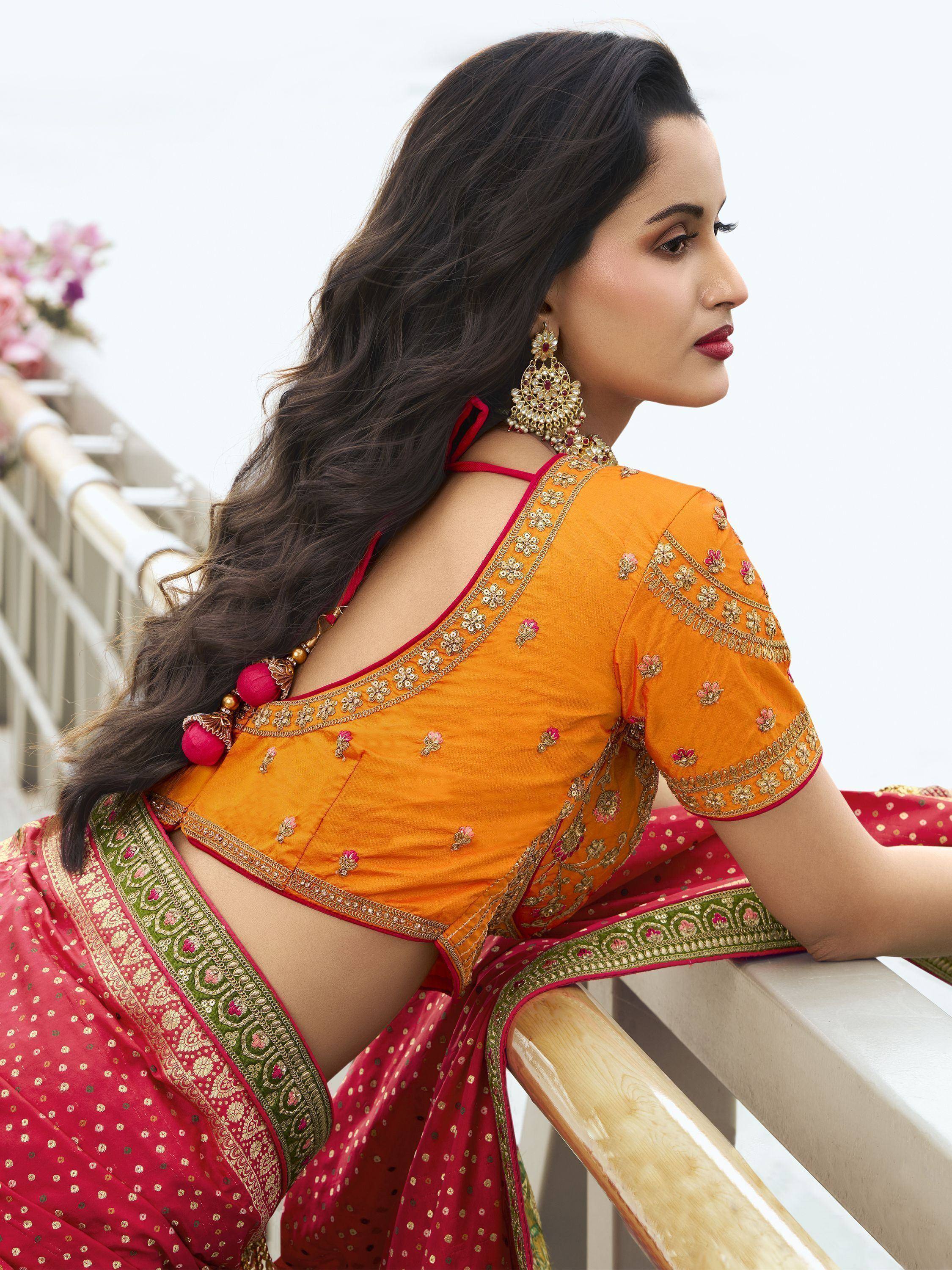Woman in vibrant orange and red embroidered saree with floral motifs and gold jewelry, showcasing Indian ethnic wear.