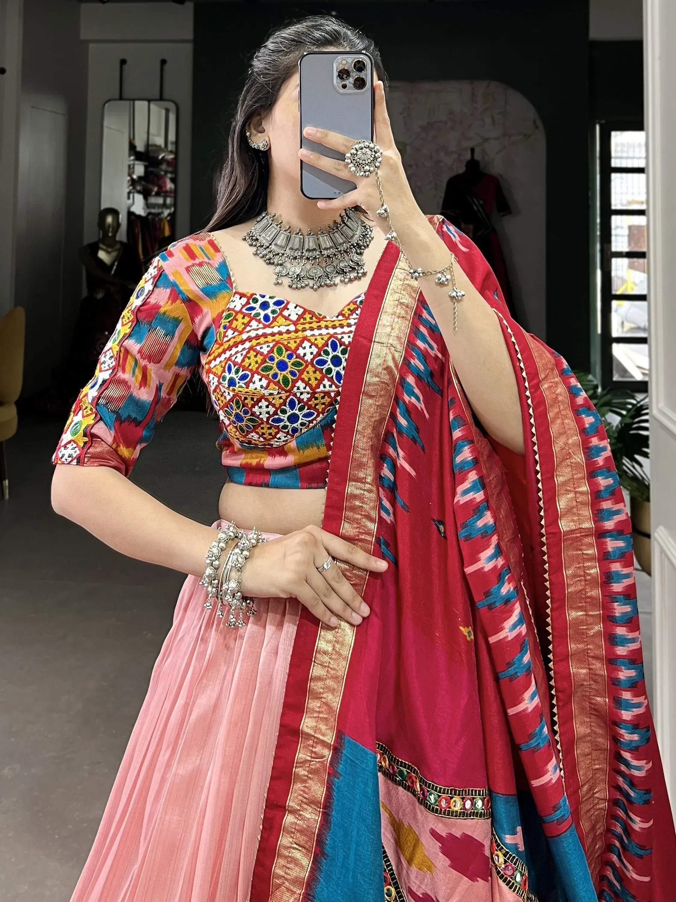 Woman in colorful embroidered lehenga choli with mirror work, pink skirt, and red dupatta, styled with silver jewelry