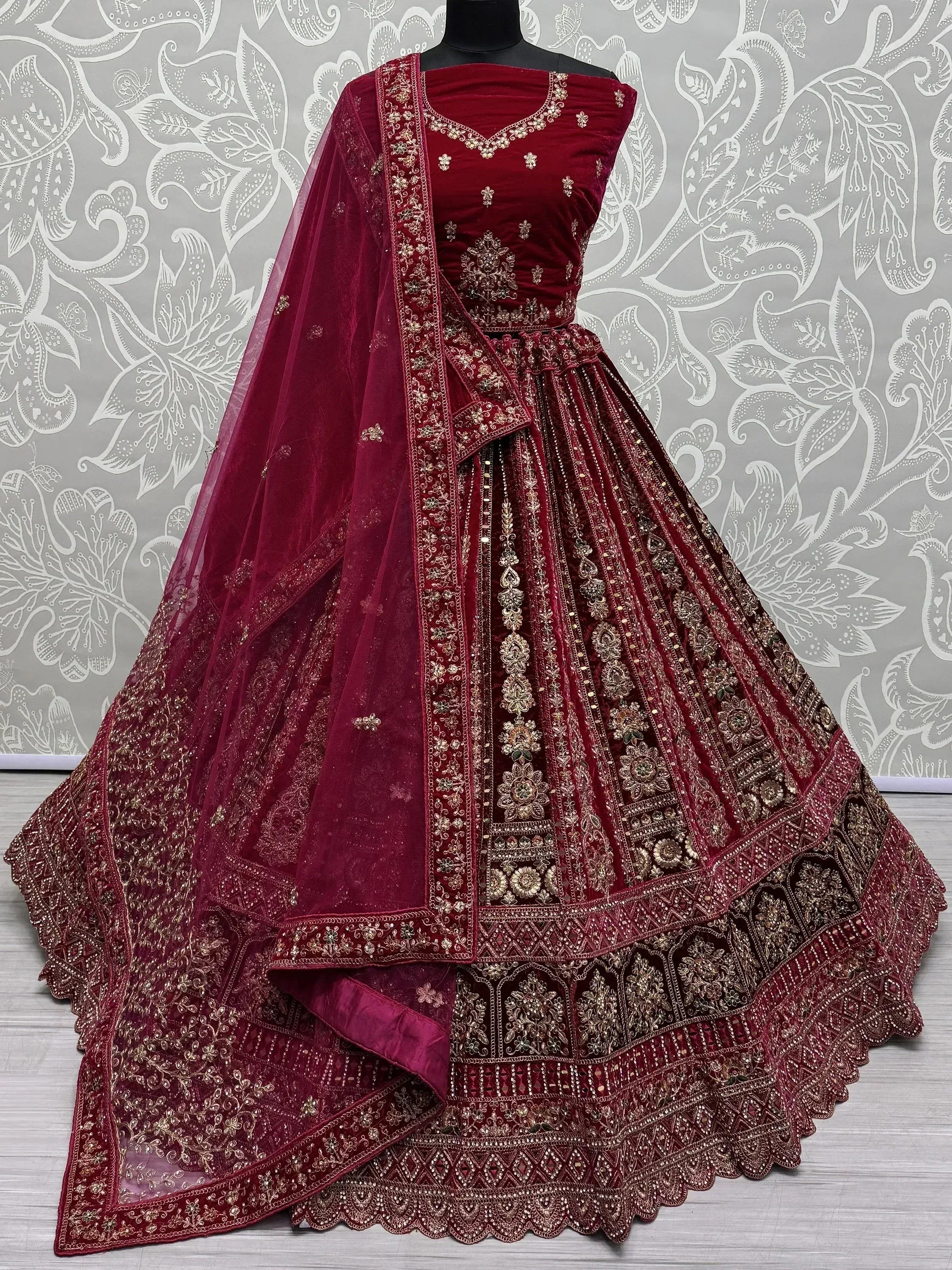 Maroon velvet designer lehenga choli with gold embroidery and net dupatta, perfect for weddings and festive occasions.