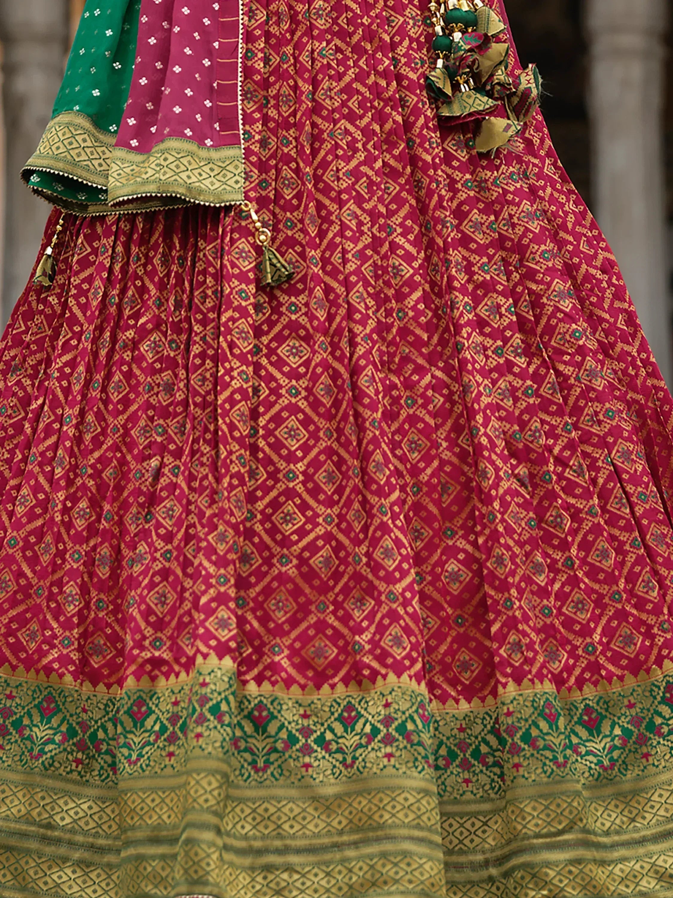 Vibrant pink and green ethnic lehenga with intricate geometric prints and gold detailing, perfect for festive occasions.