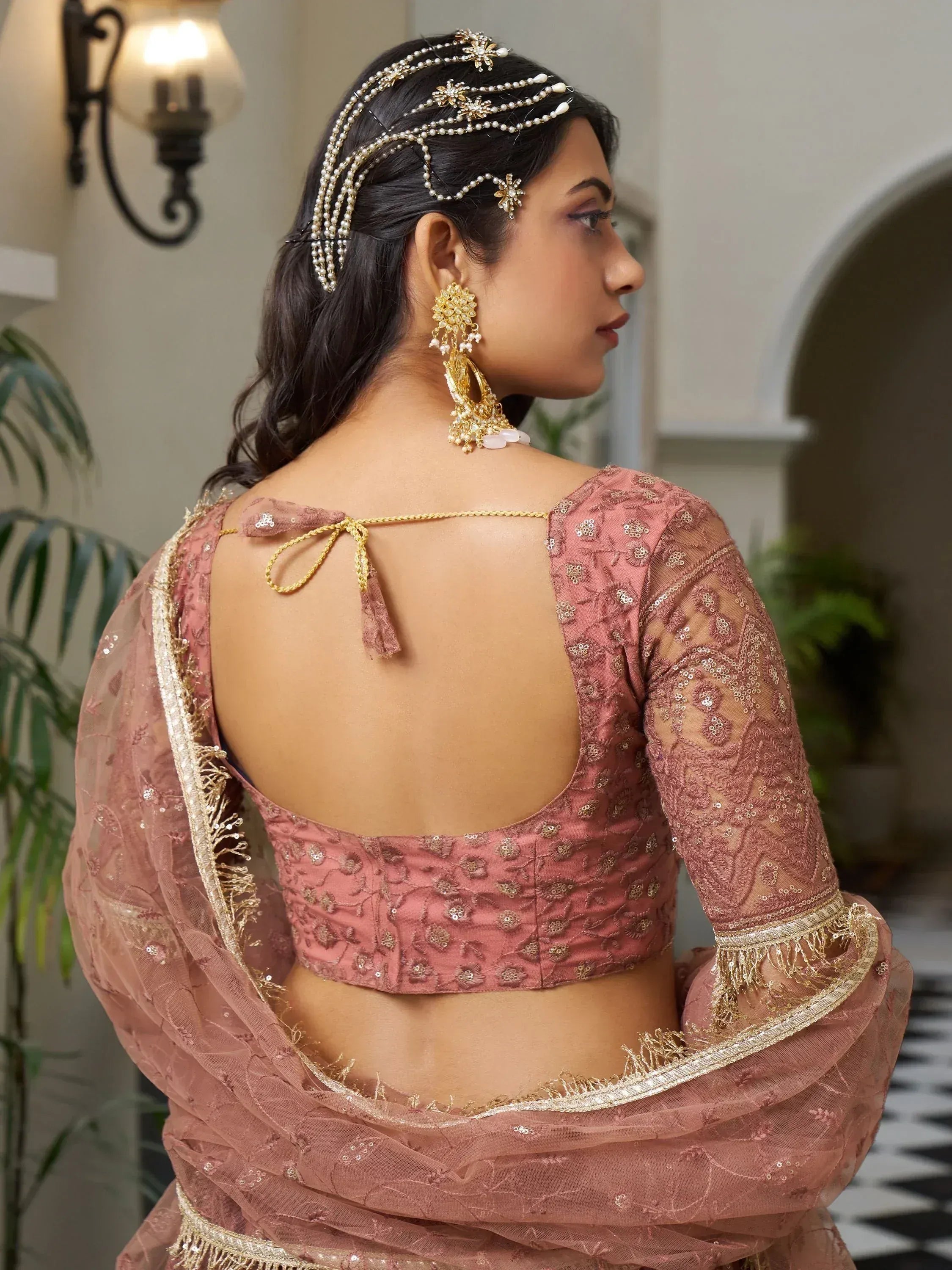 Pink embroidered lehenga choli with back tie, gold jewelry, and pearl hair accessory for Indian ethnic wear