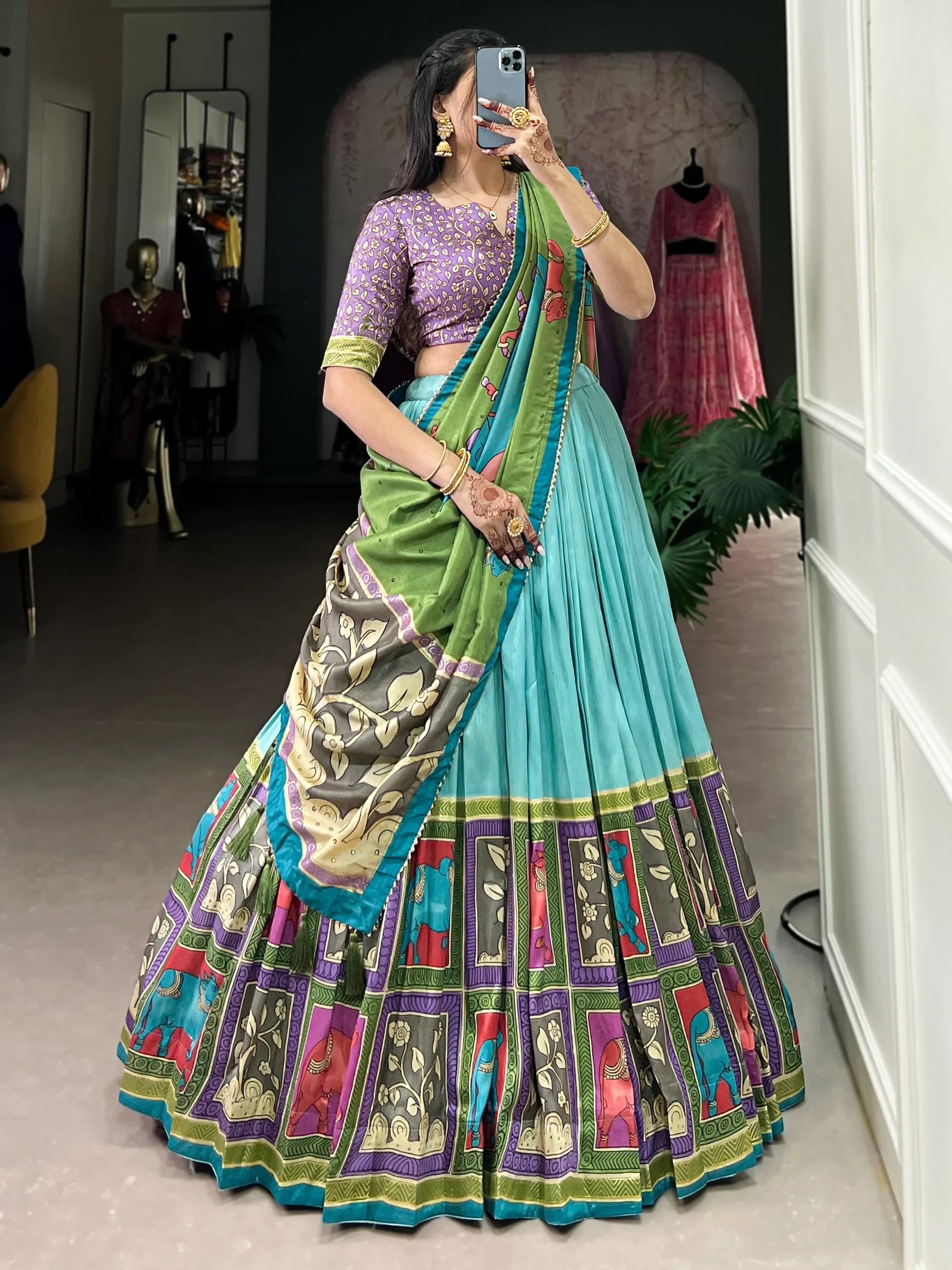 Woman in colorful printed lehenga choli with purple blouse, green dupatta, and elephant motifs, taking mirror selfie
