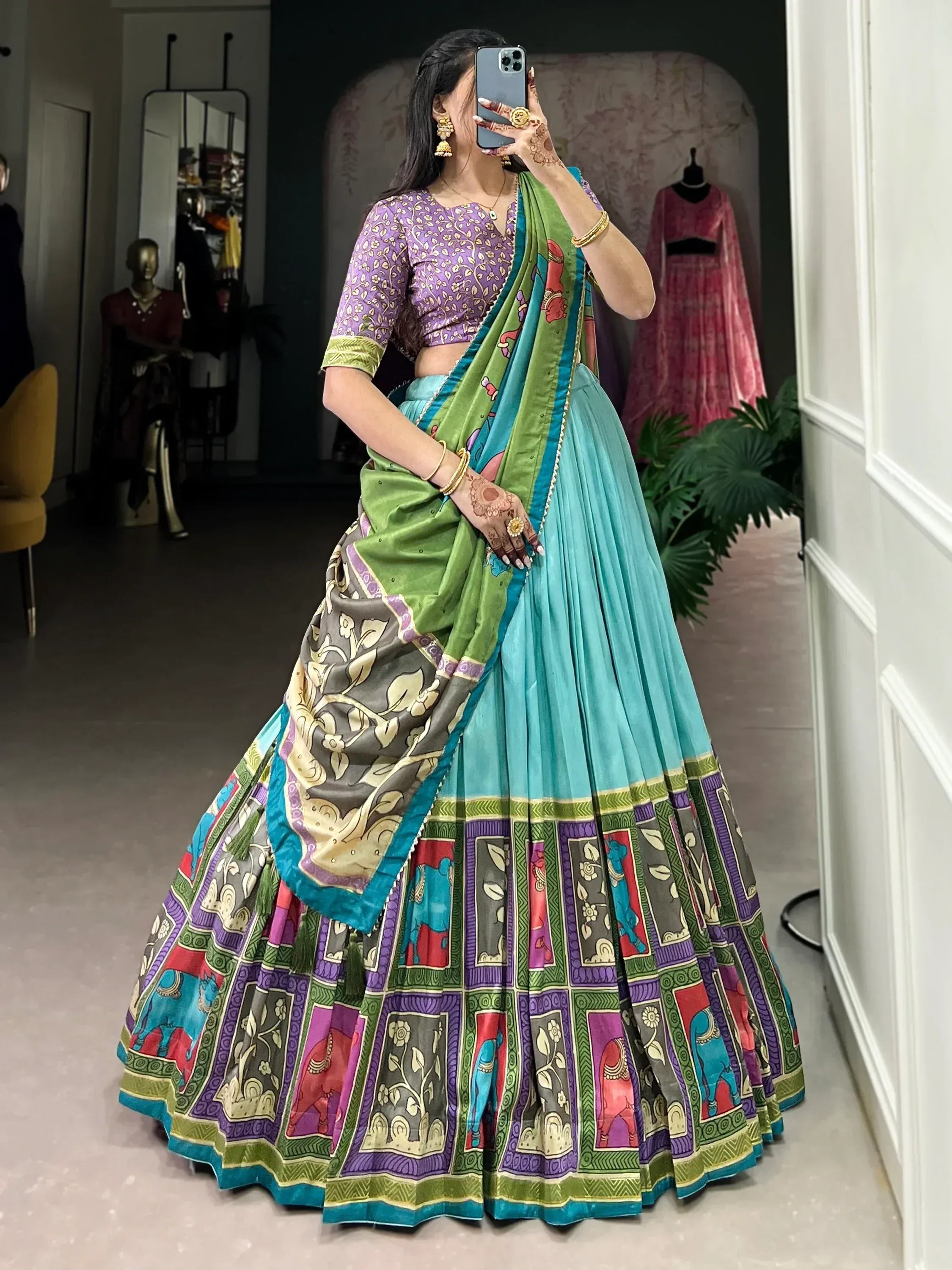 Woman in colorful printed lehenga choli with purple blouse, green dupatta, and elephant motifs, taking mirror selfie