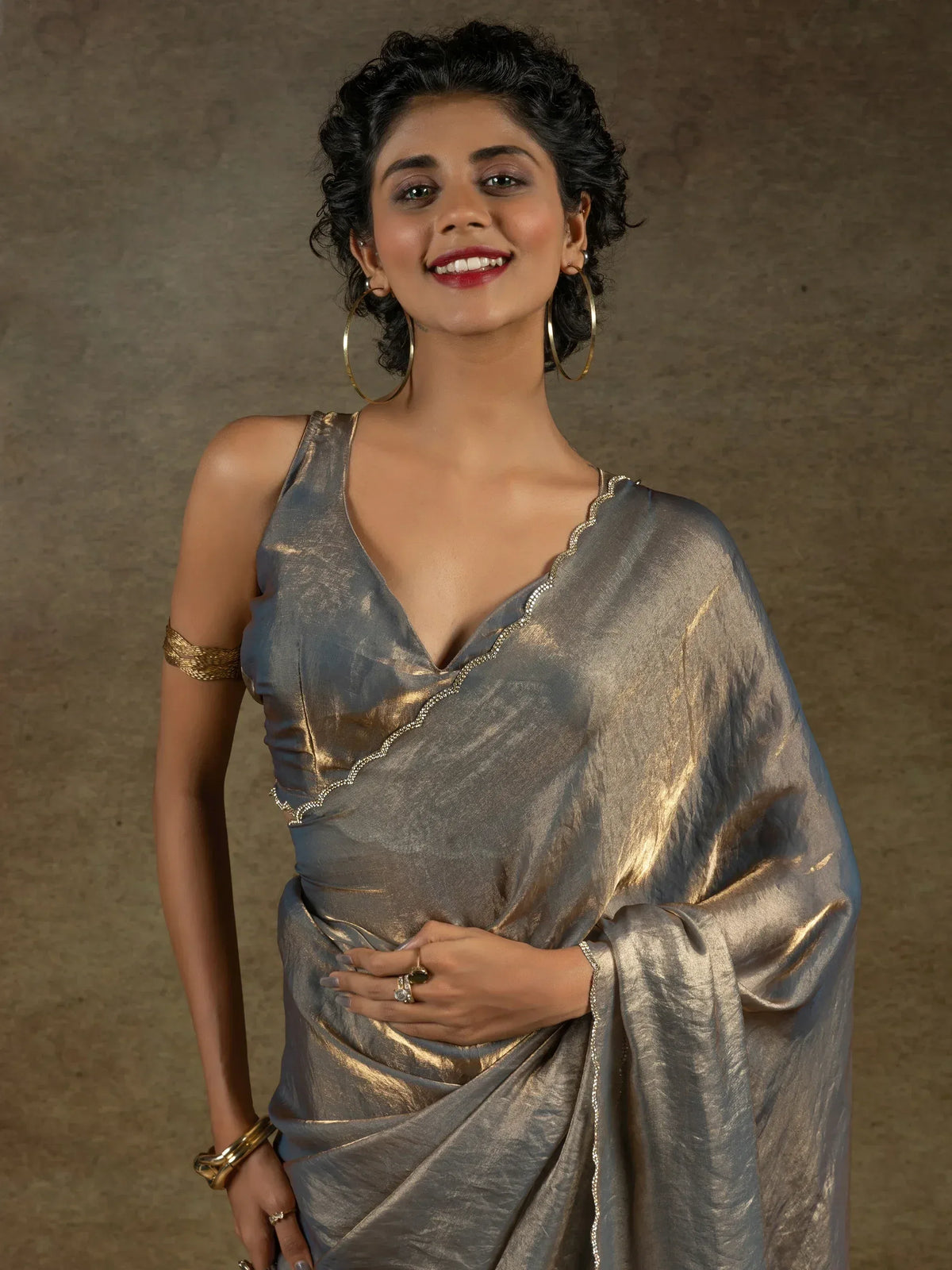 Woman in shimmering silver saree with gold trim, styled with hoop earrings and arm cuff for ethnic occasions