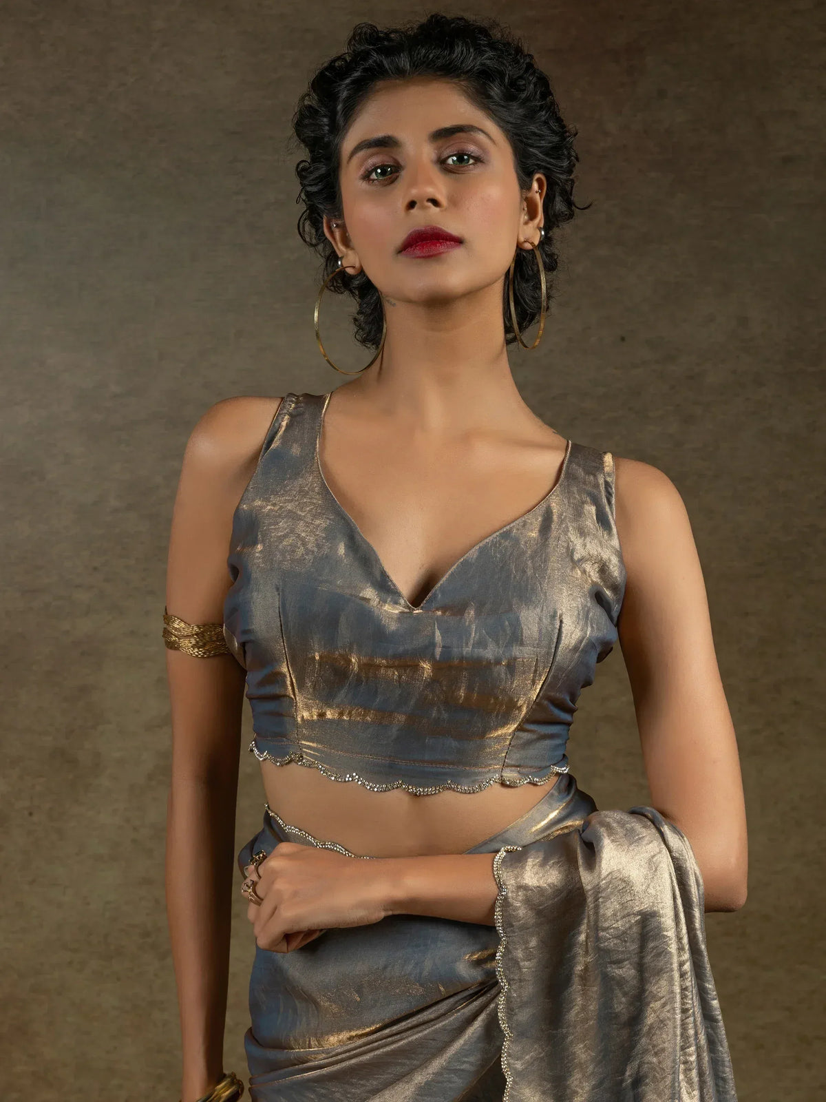 Woman in metallic grey saree with gold accents and scalloped blouse, styled with hoop earrings for ethnic wear.