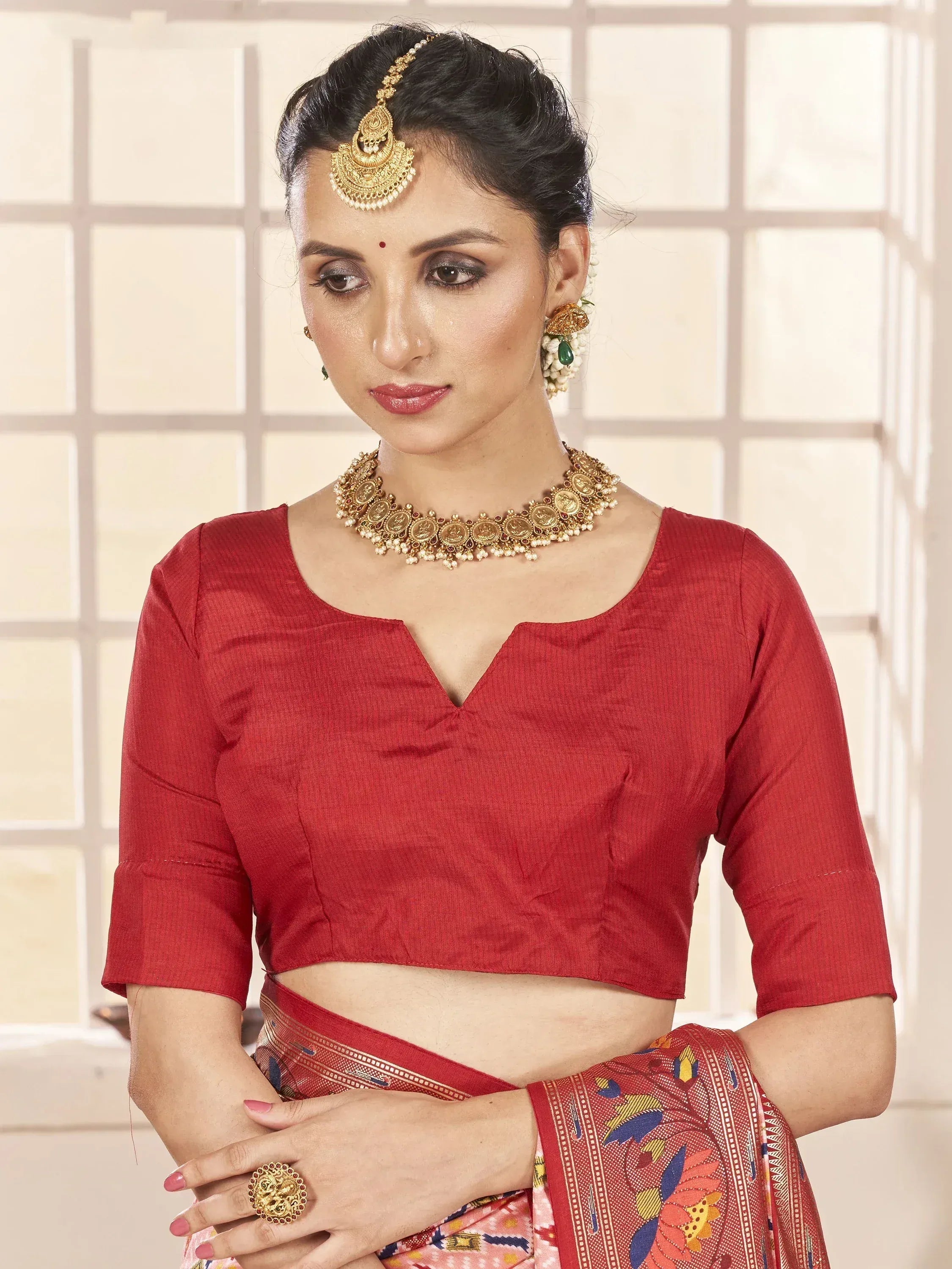 Woman in red ethnic blouse with gold jewelry and floral saree, traditional Indian attire