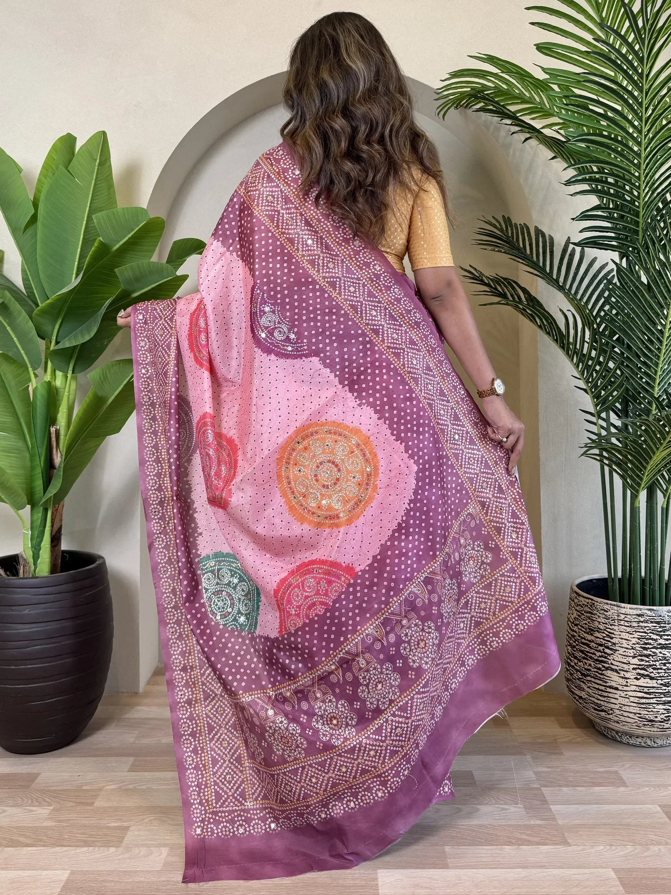 Woman showcasing vibrant pink and purple ethnic saree with mirror work and bandhani print, perfect for Indian occasions.