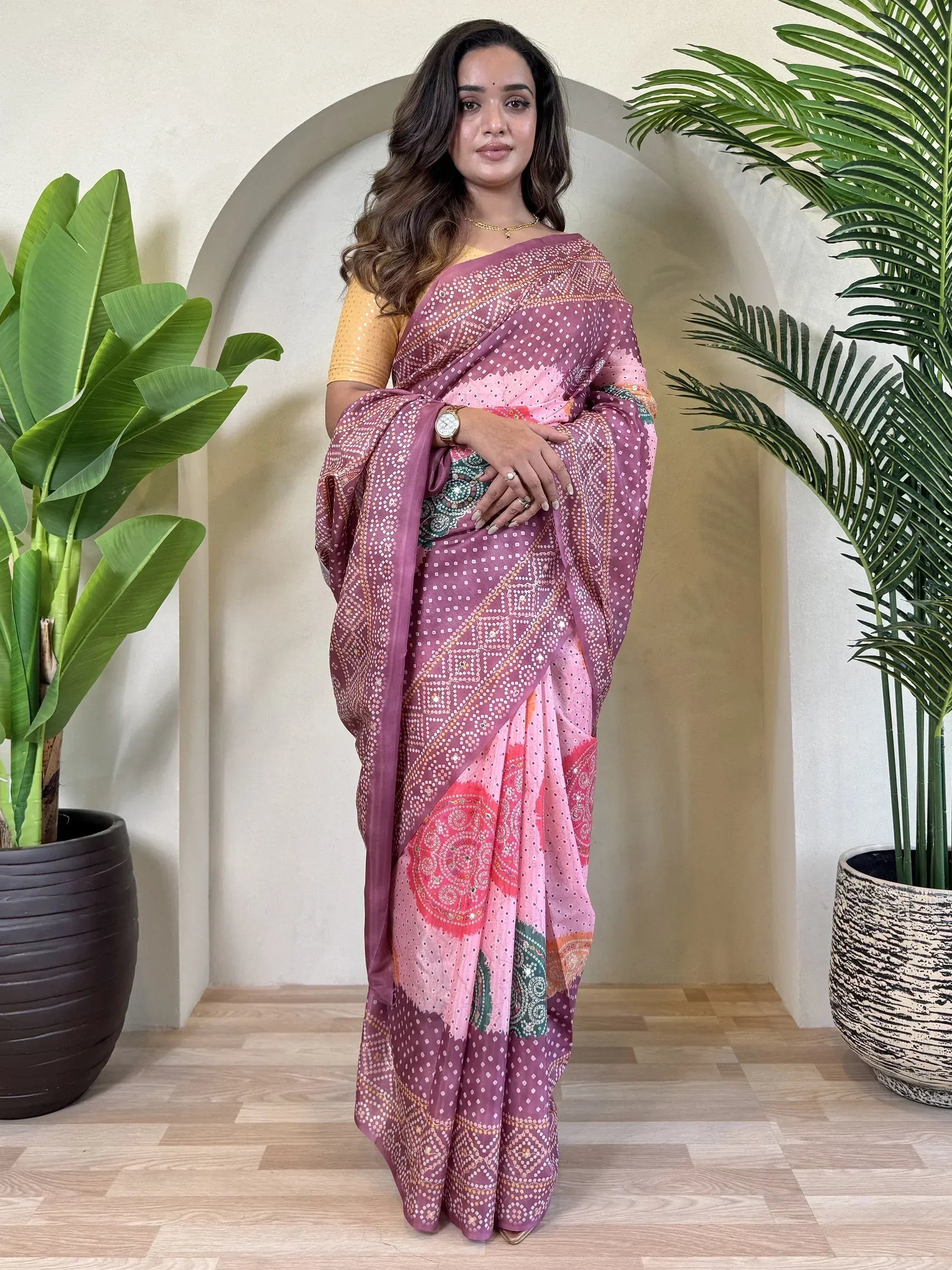 Woman in pink and purple printed saree with yellow blouse, standing near plants