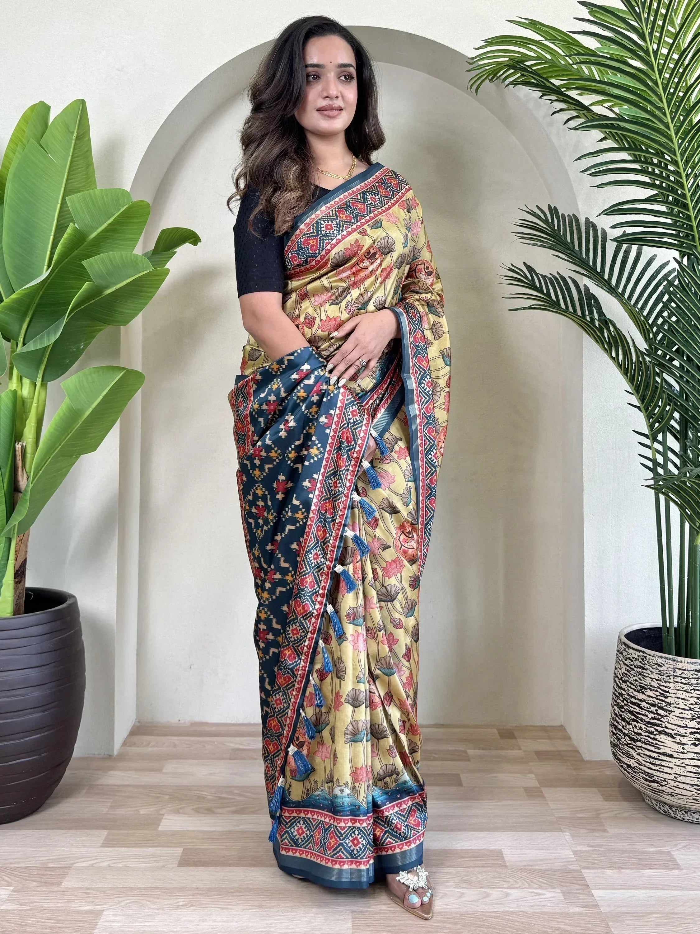 Woman wearing floral print ethnic saree with blue border and tassels, paired with black blouse