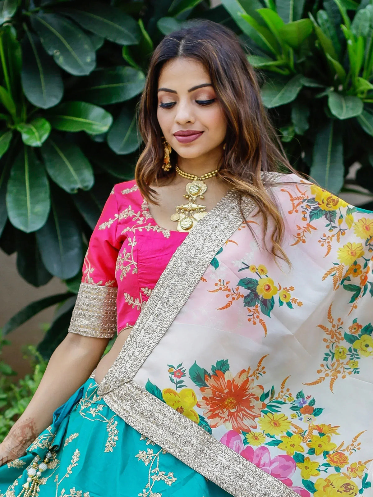 Woman in vibrant floral saree with pink blouse and gold jewelry, perfect for ethnic occasions.