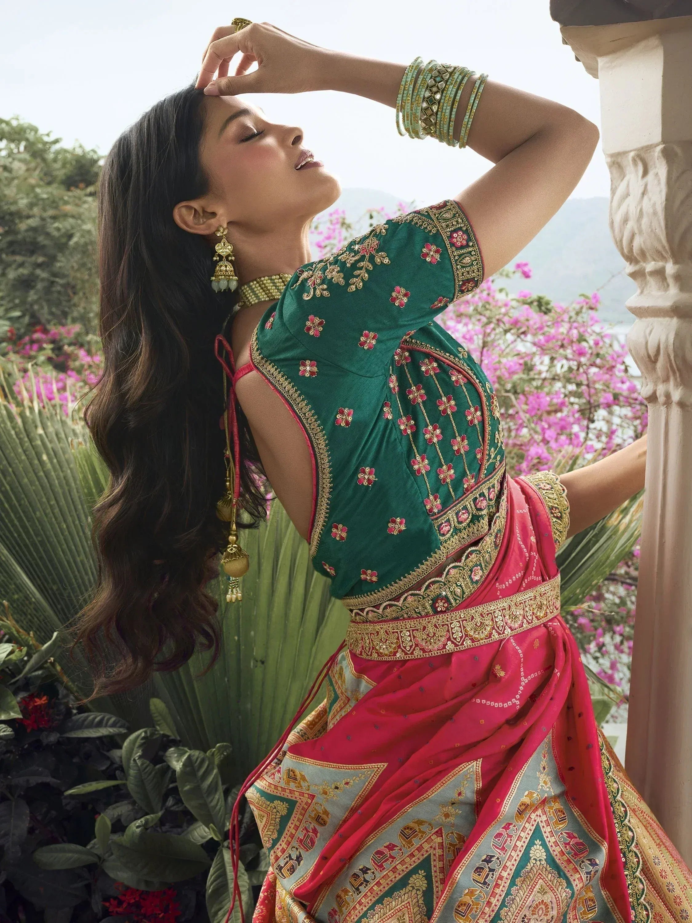 Woman in green and pink embroidered saree with gold jewelry, garden backdrop