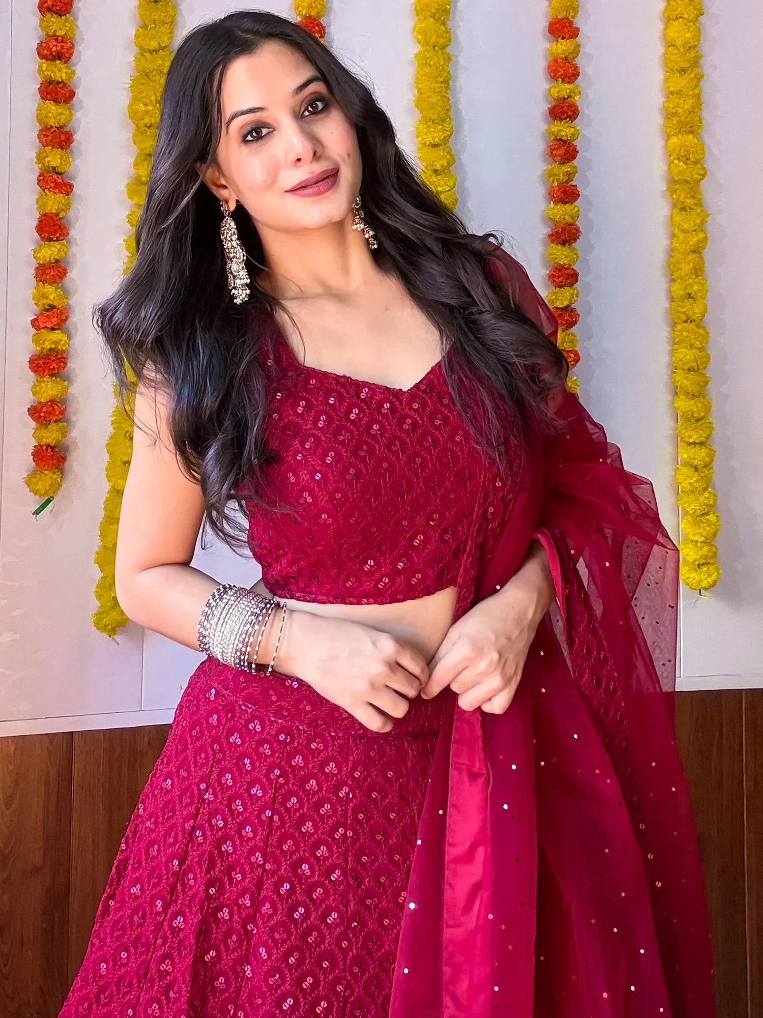 Woman in maroon sequined lehenga choli with floral garlands, perfect for Indian ethnic occasions