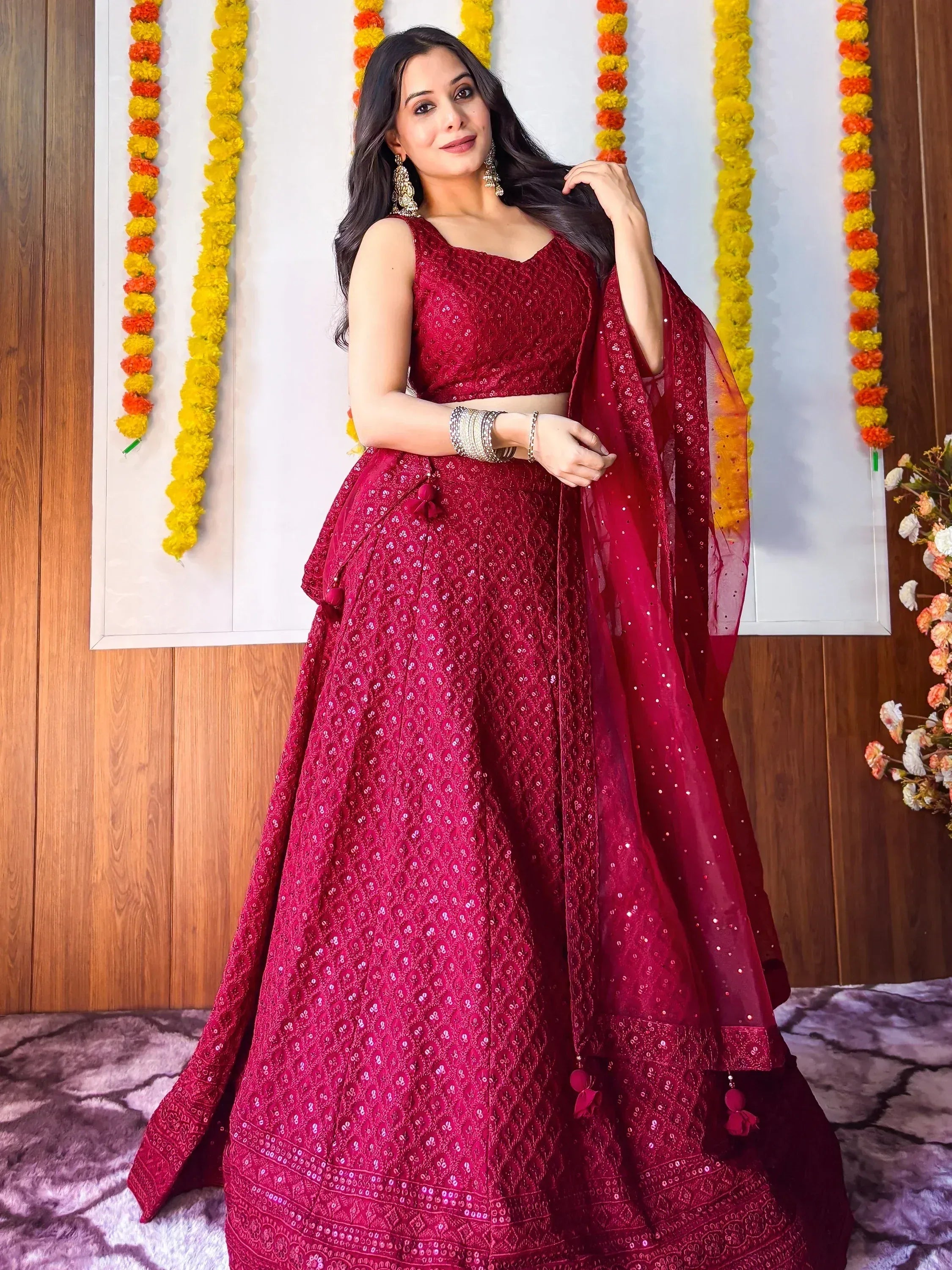 Woman in maroon embroidered lehenga choli with floral garlands, perfect for Indian ethnic wear occasions