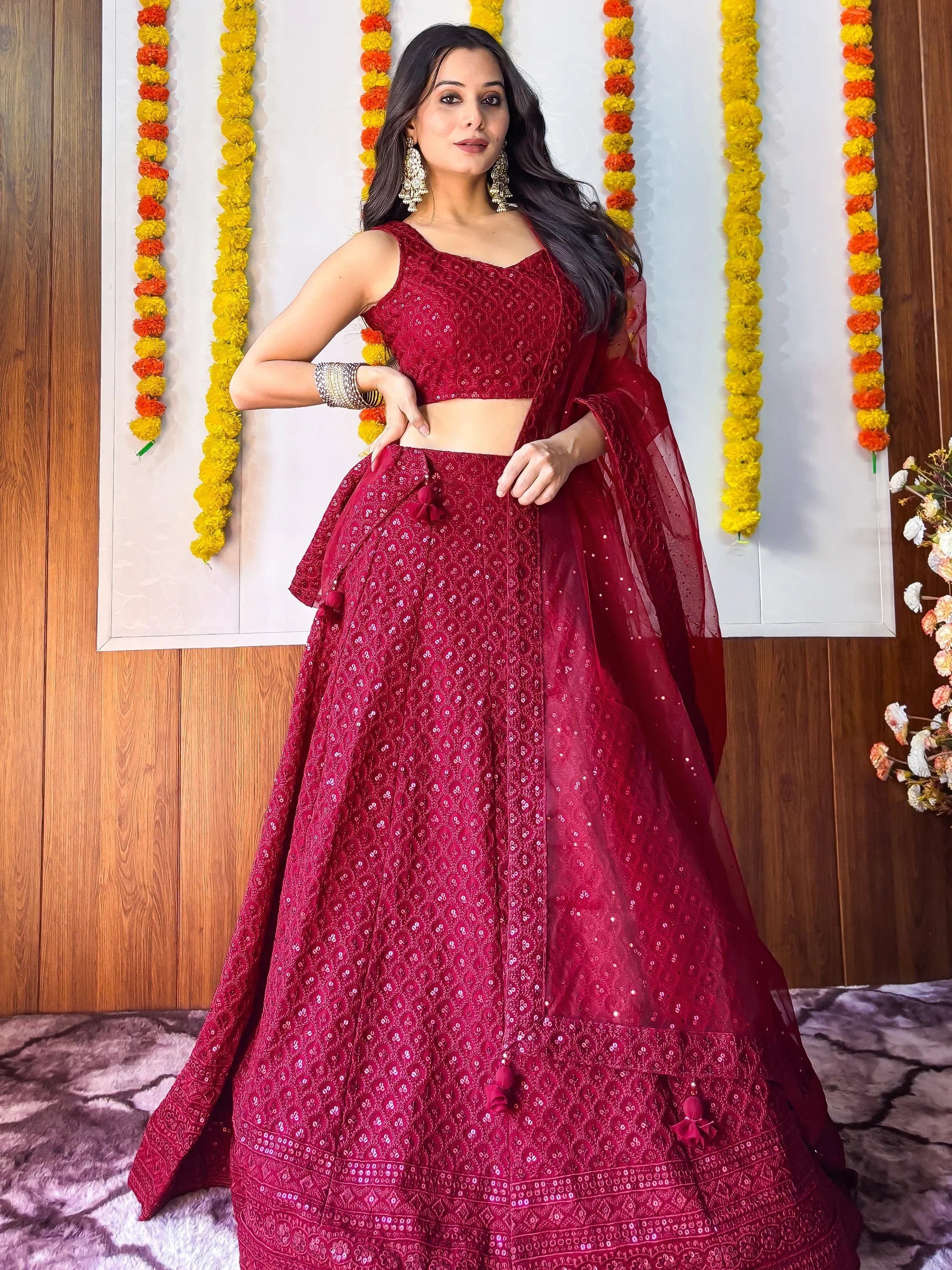 Woman in maroon designer lehenga choli with floral garlands, perfect for Indian ethnic wear events