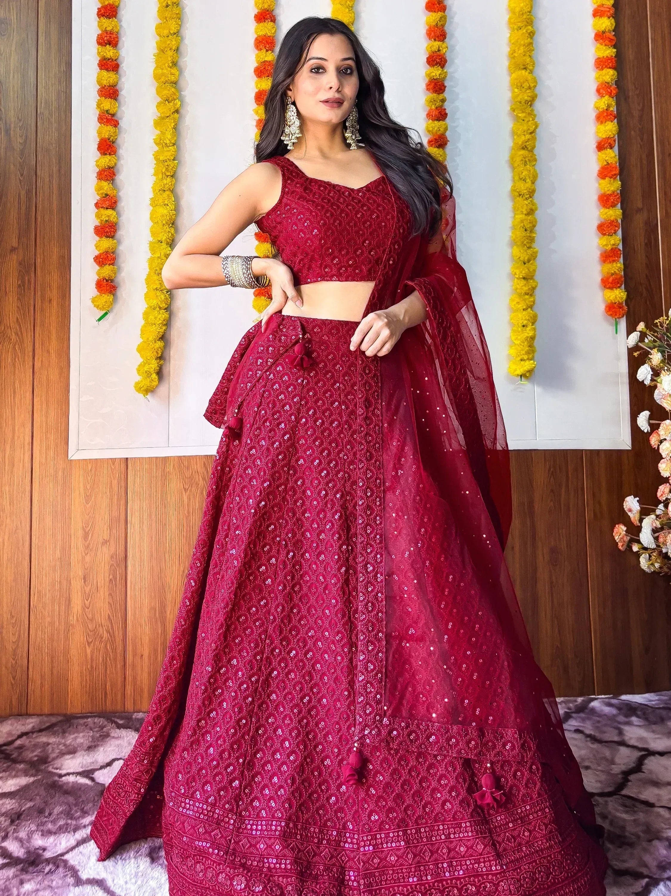 Woman in maroon designer lehenga choli with floral garlands, perfect for Indian ethnic wear events