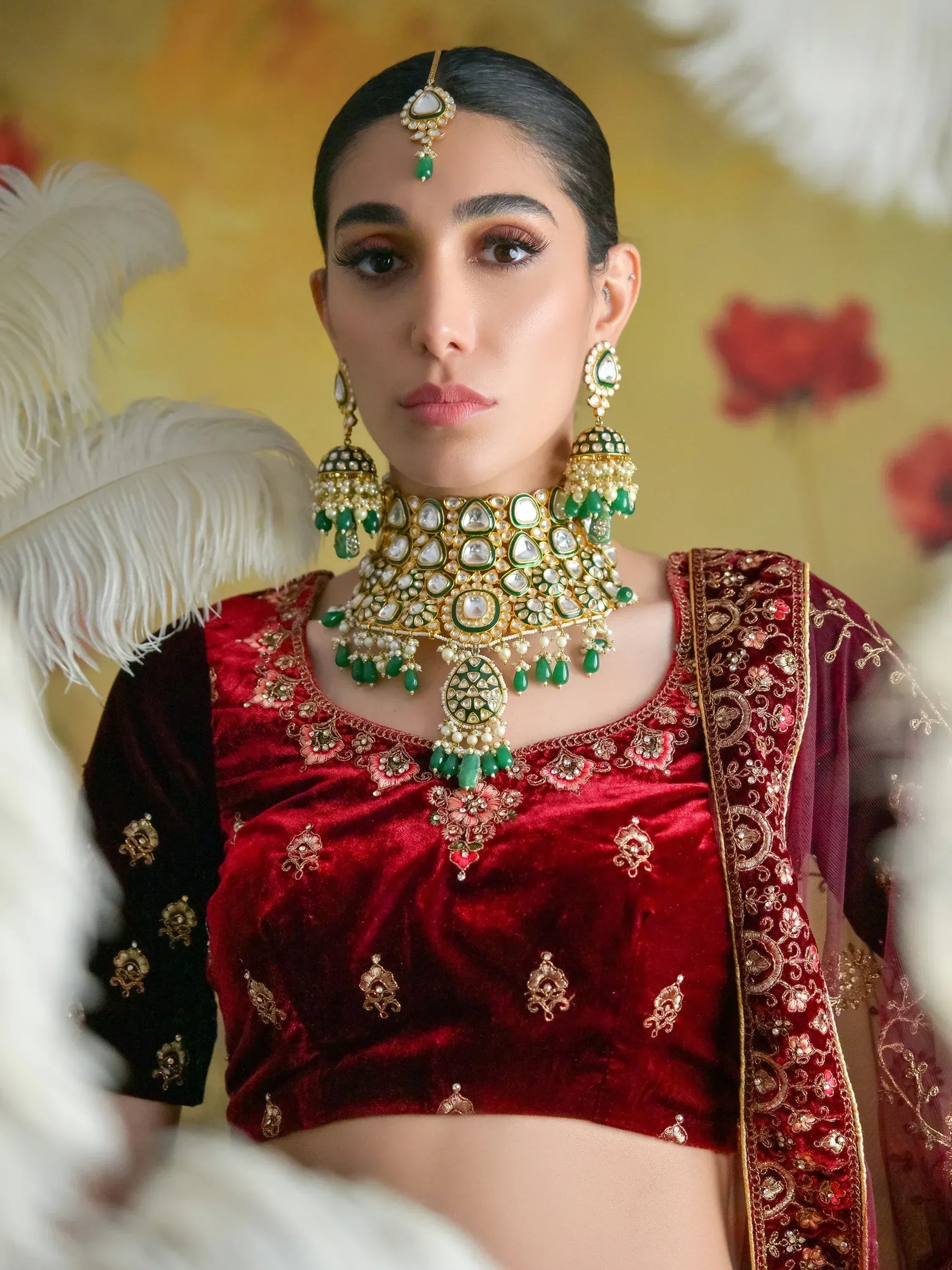 Woman in red velvet ethnic blouse with green and gold jewelry, perfect for Indian weddings or festive occasions.