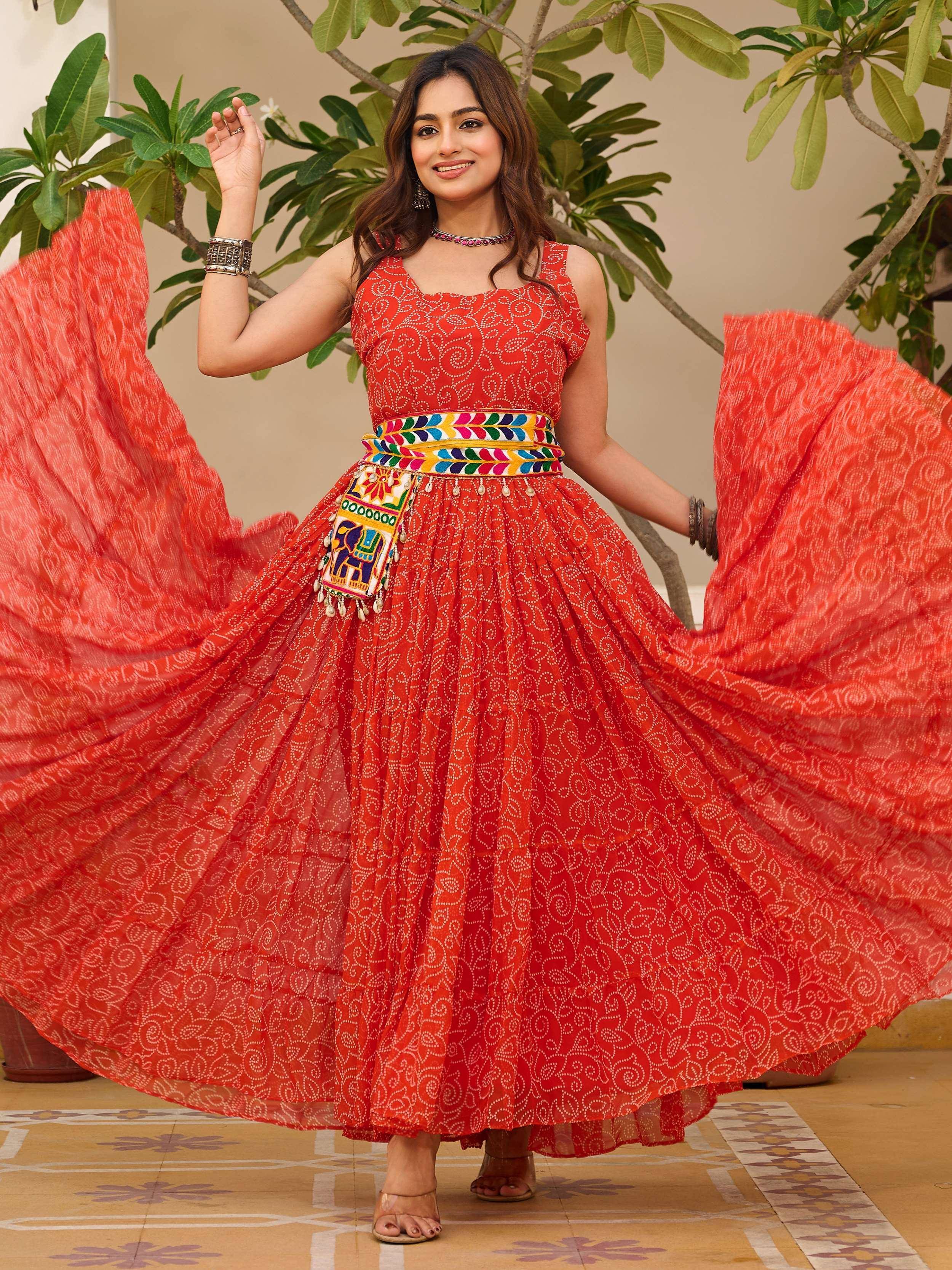 Woman in vibrant red ethnic gown with printed patterns and colorful belt, twirling outdoors