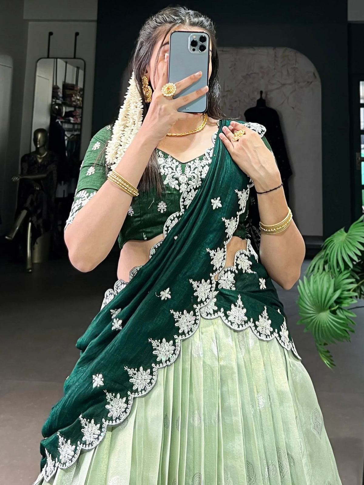 Emerald green velvet lehenga choli with white floral embroidery, paired with gold jewelry and floral garland