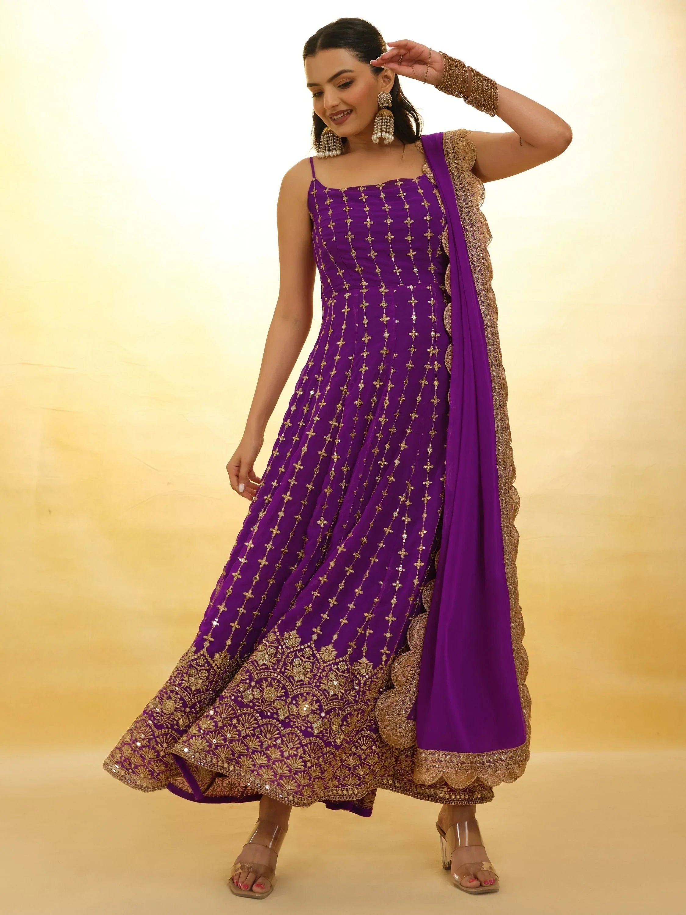 Woman wearing a purple embroidered Anarkali gown with gold detailing and matching dupatta