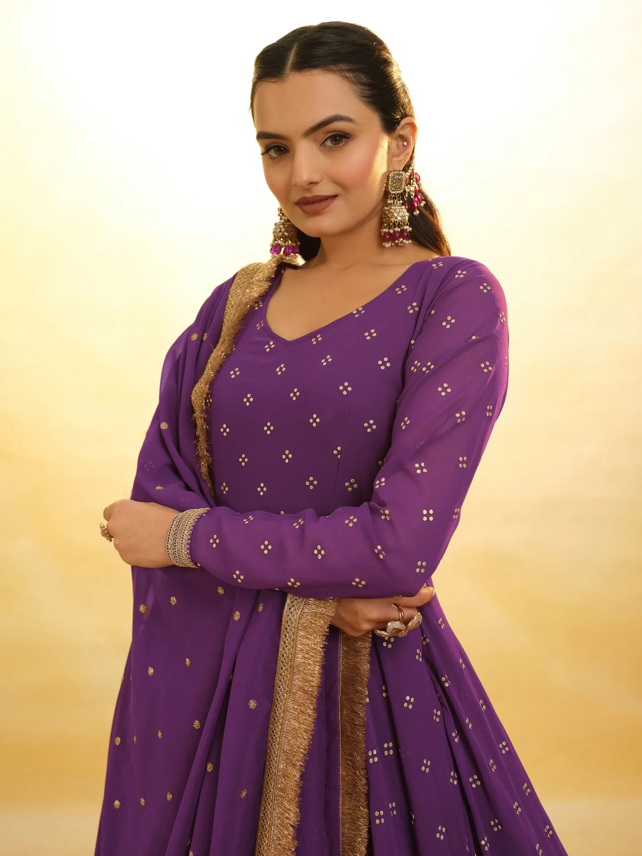 Woman wearing a purple ethnic gown with gold embroidery and dupatta, statement earrings