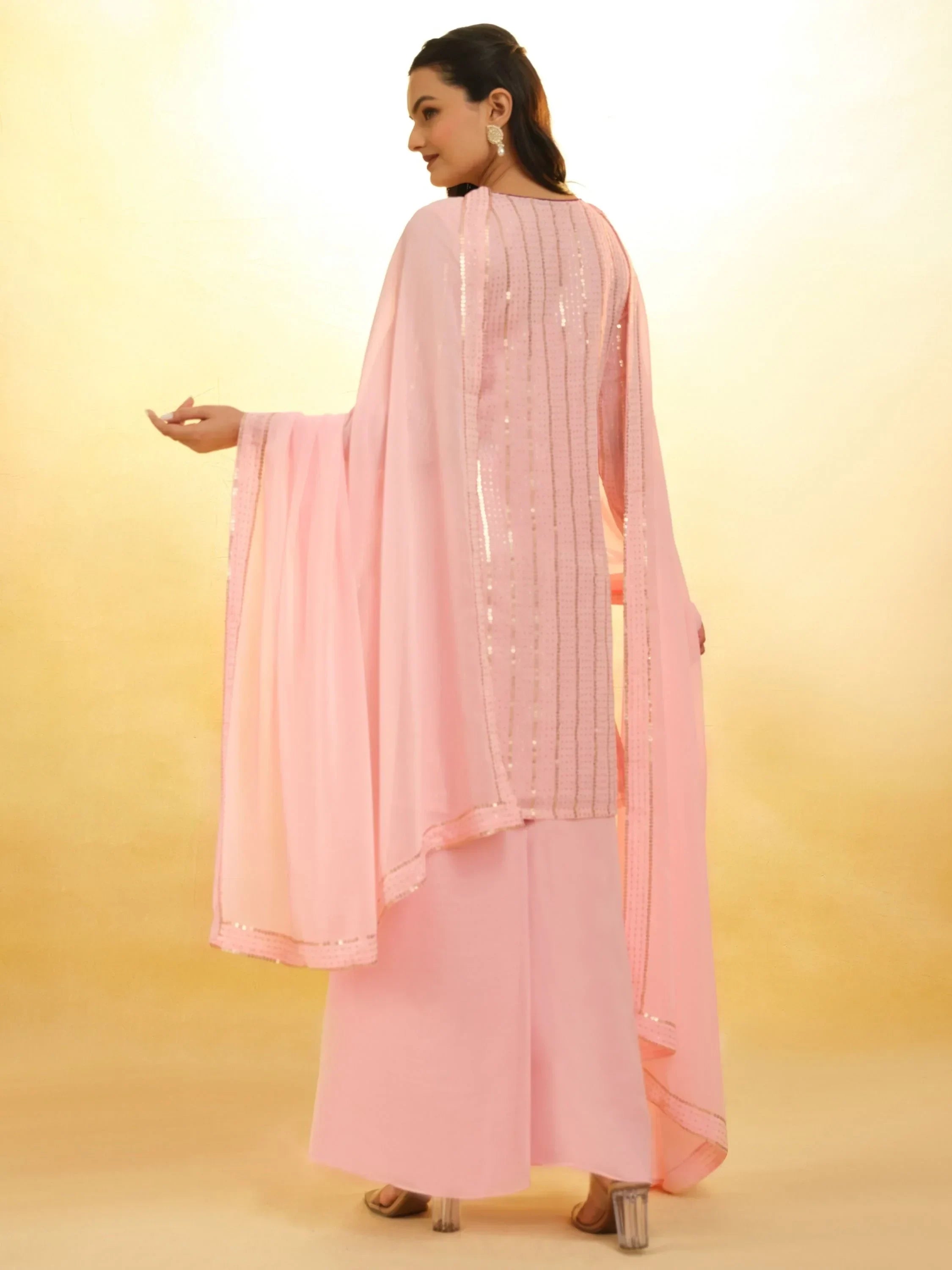 Woman in light pink palazzo salwar kameez set with sequin detailing, back view