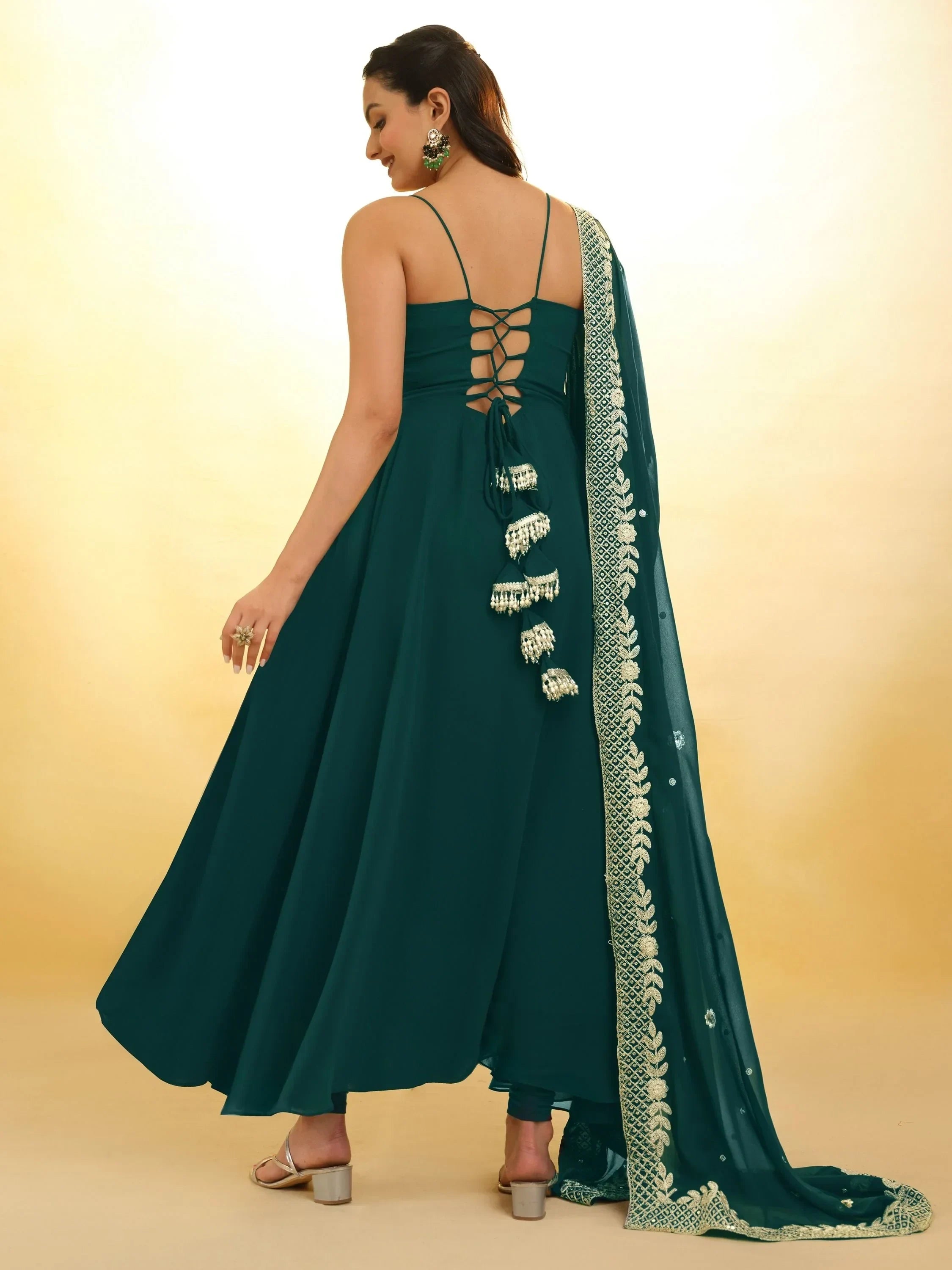 Woman in teal anarkali suit with strappy back, tassel accents, and embroidered dupatta