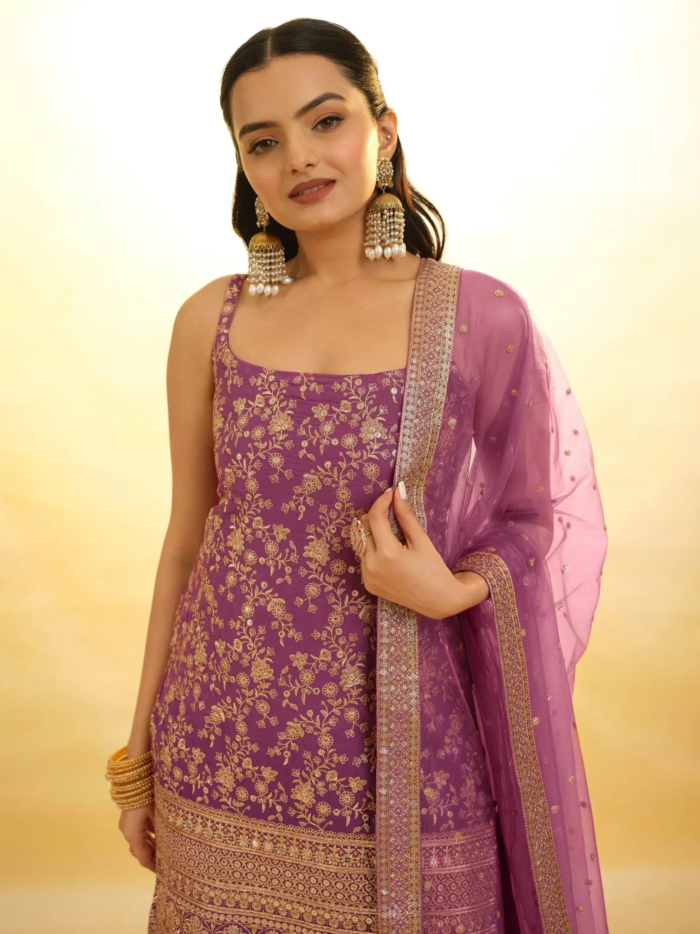 Purple embroidered ethnic gown with gold floral work and matching dupatta, styled with jhumka earrings