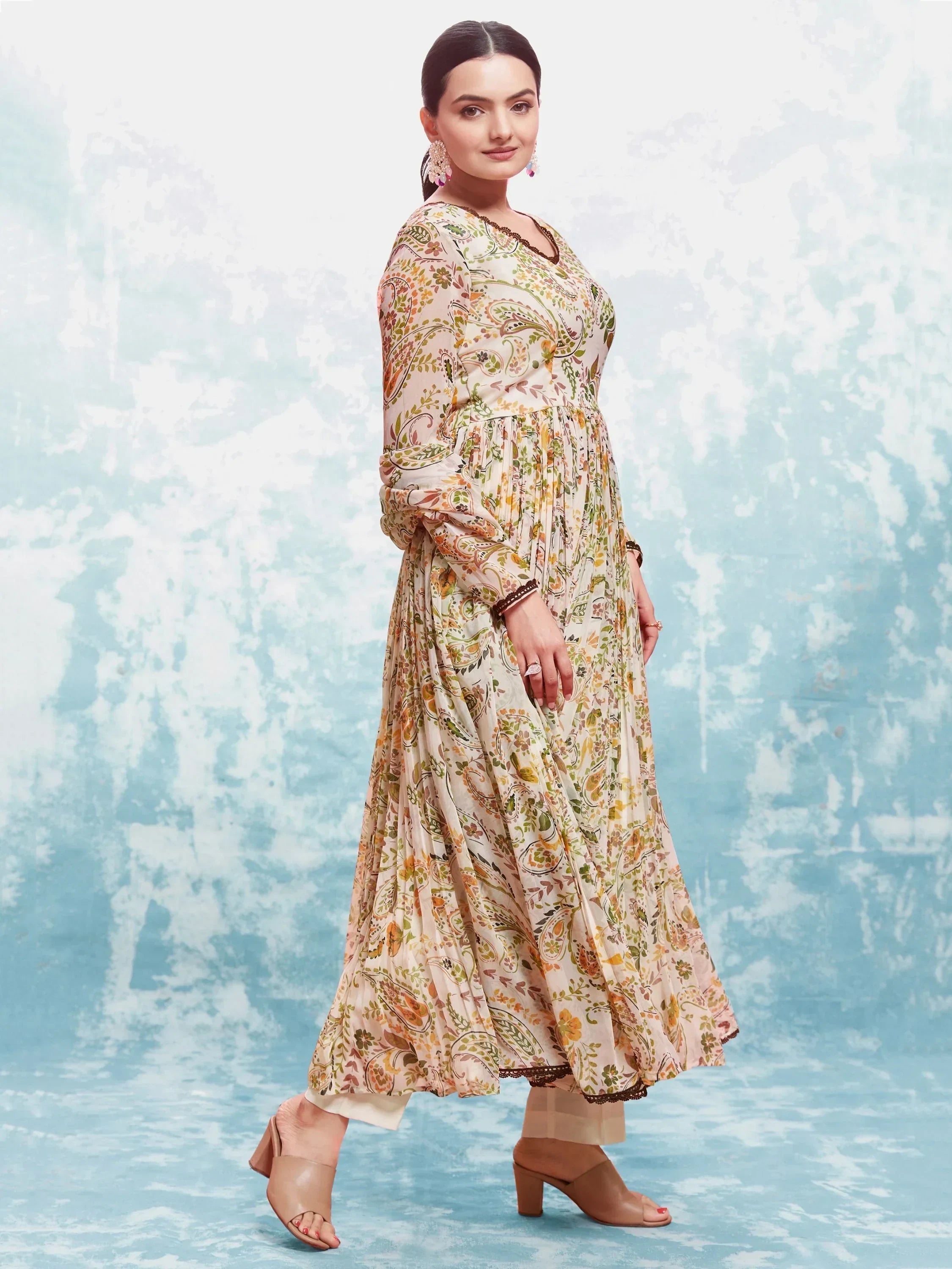 Woman wearing a floral ethnic gown with long sleeves and block heels, against blue background