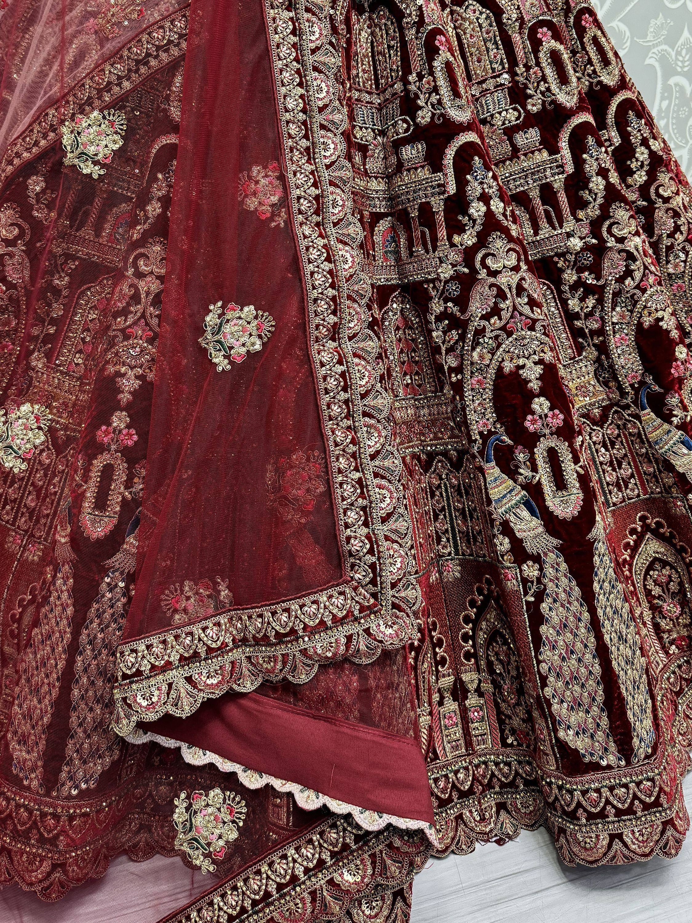 Luxury maroon velvet lehenga choli with intricate gold embroidery, peacock motifs, and floral detailing for Indian weddings.