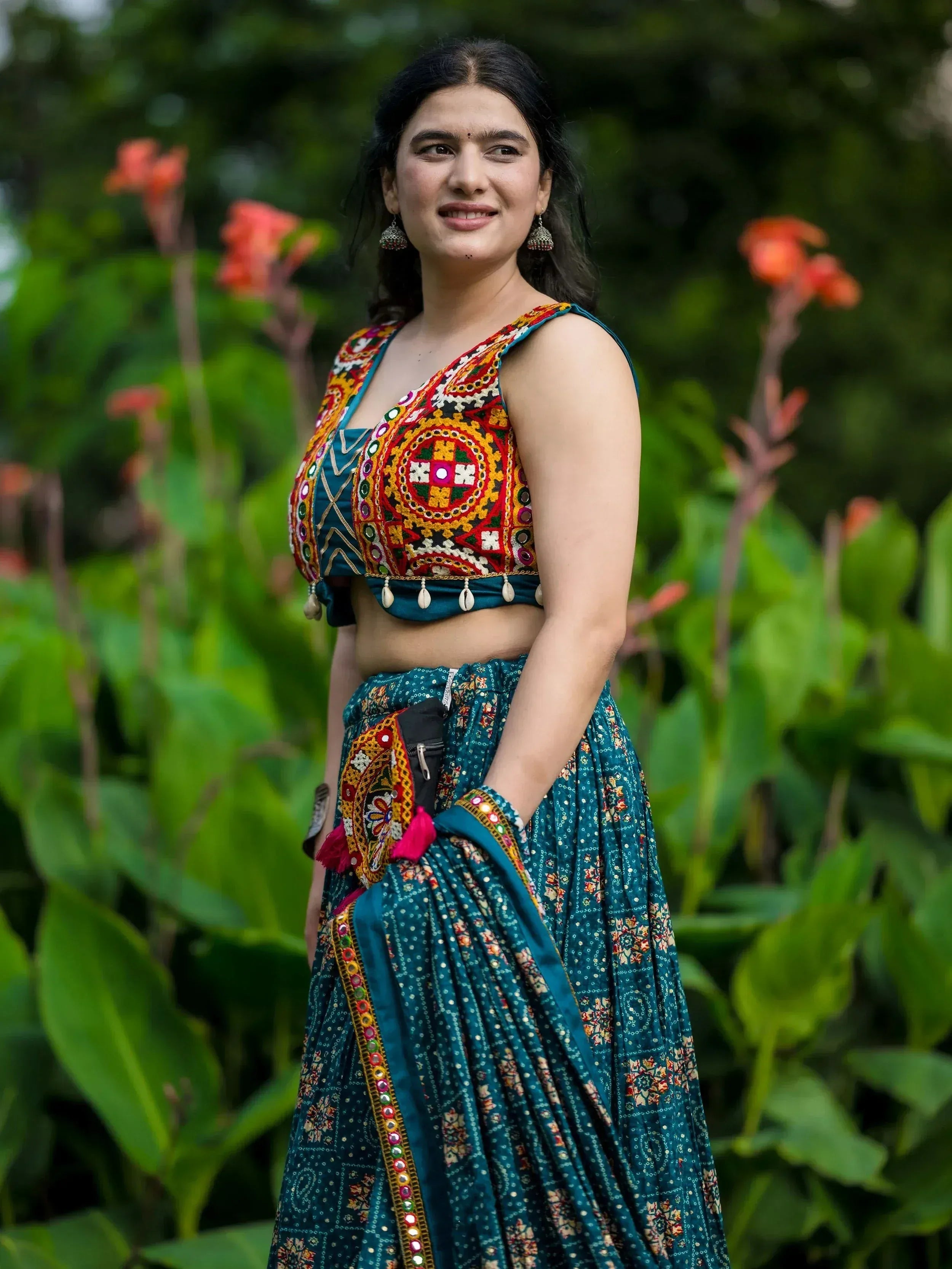 Woman in vibrant teal Indian ethnic wear with mirror work blouse and floral skirt, garden setting