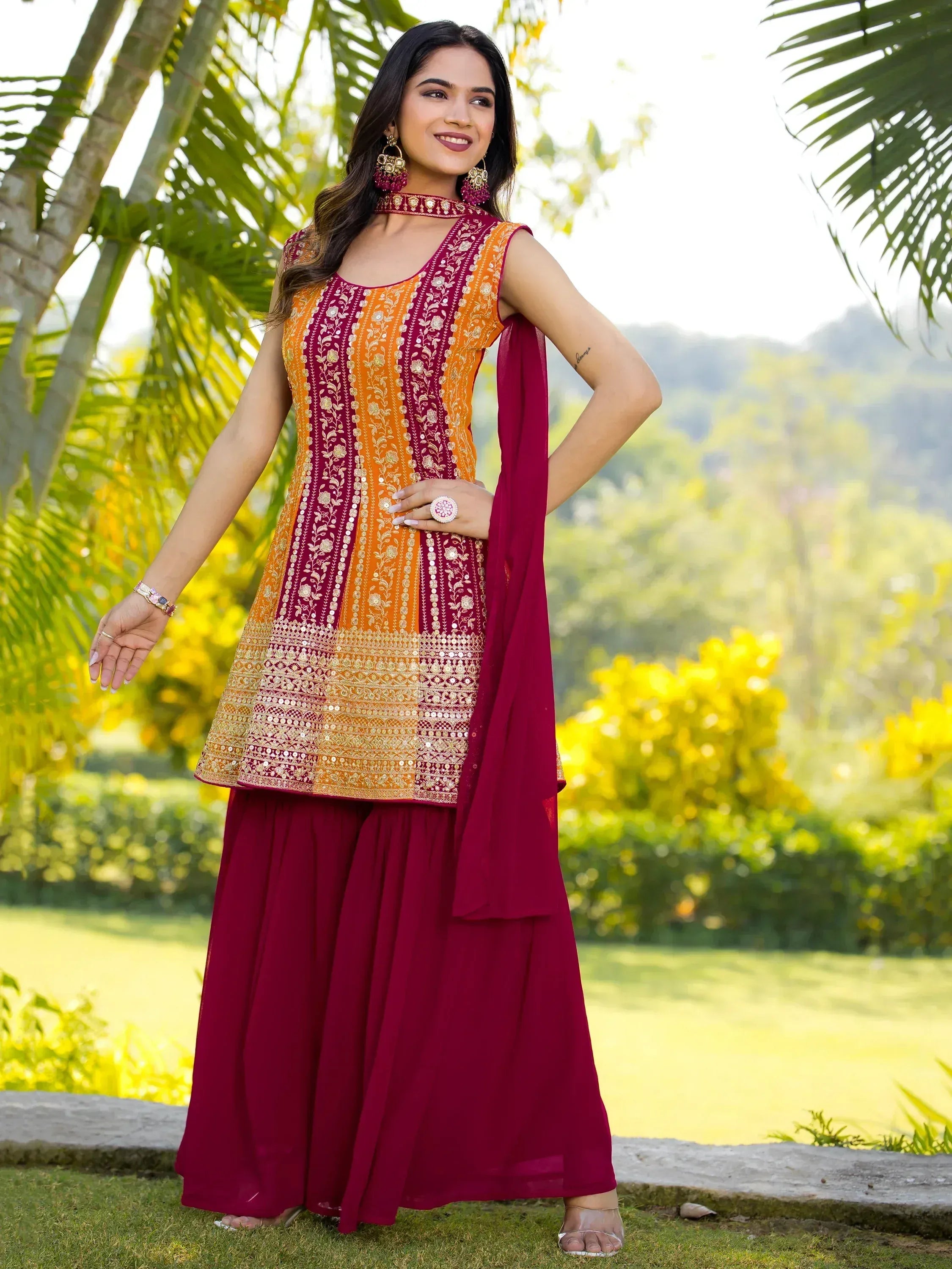 Woman in maroon and orange embroidered ethnic salwar kameez with dupatta, outdoor garden setting