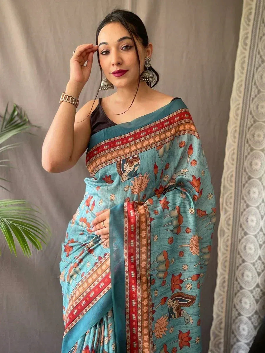 Woman wearing turquoise floral print saree with red border, styled with black blouse and jhumka earrings