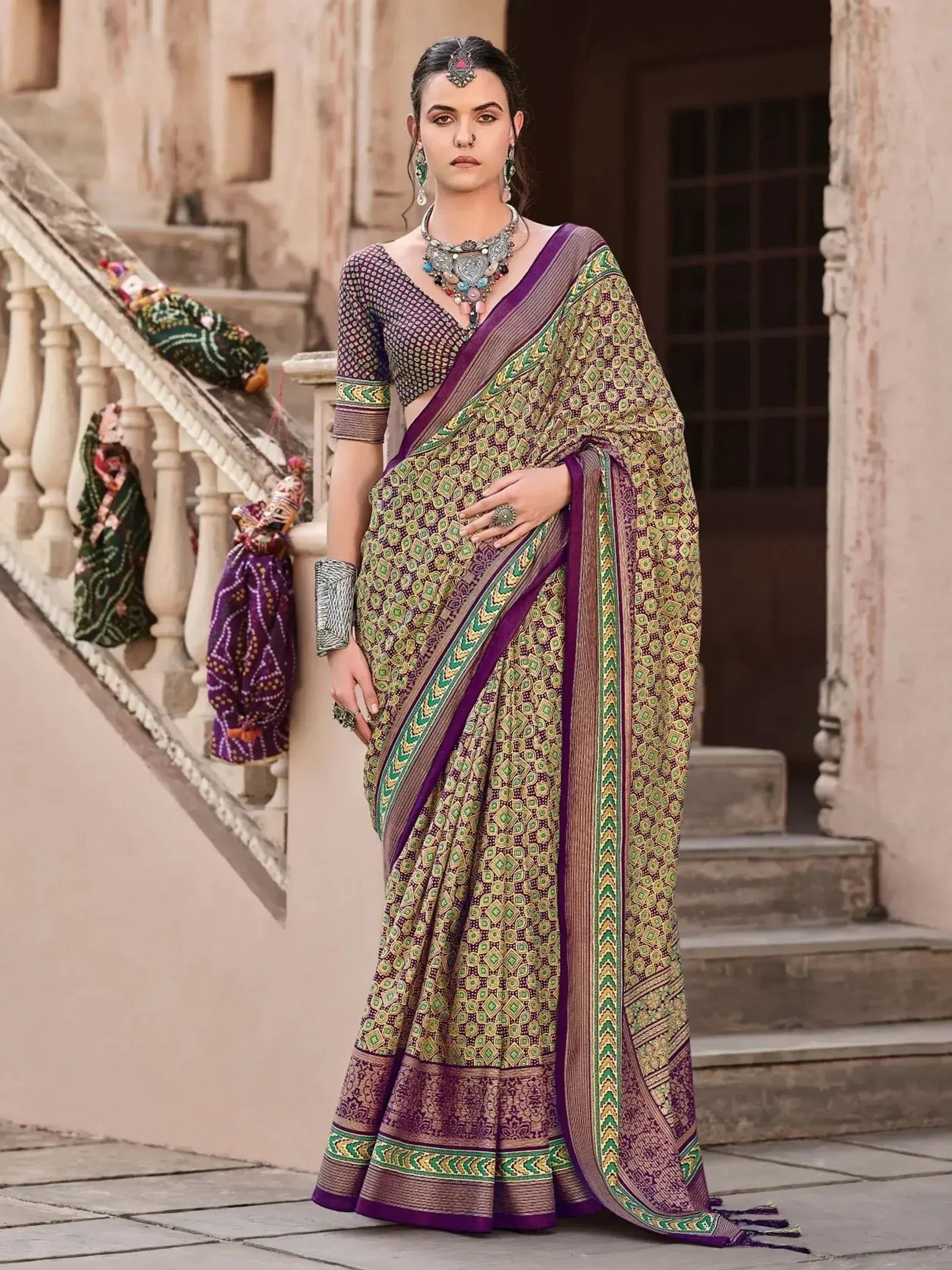 Woman in purple and green printed saree with ethnic jewelry, standing on stone steps