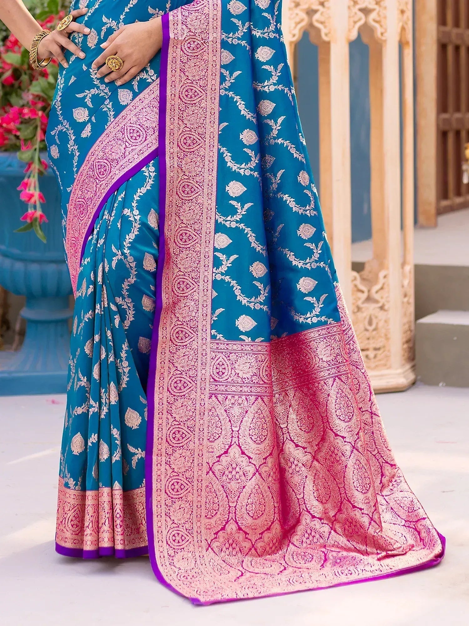 Teal designer saree with pink gold zari border, floral motifs, and purple trim for ethnic occasions