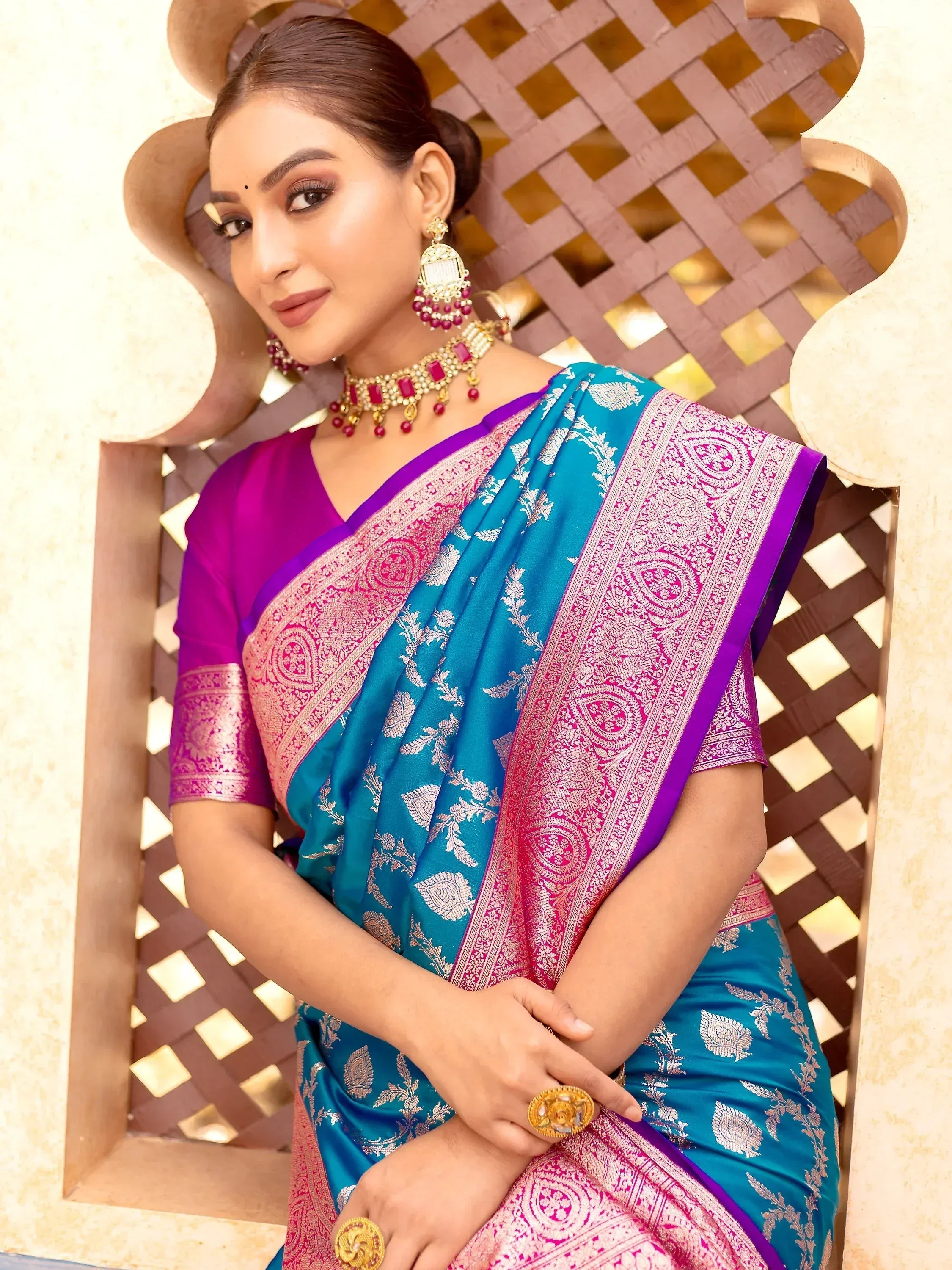 Woman in vibrant blue and pink designer saree with gold embroidery, paired with traditional jewelry, perfect for ethnic occasions.