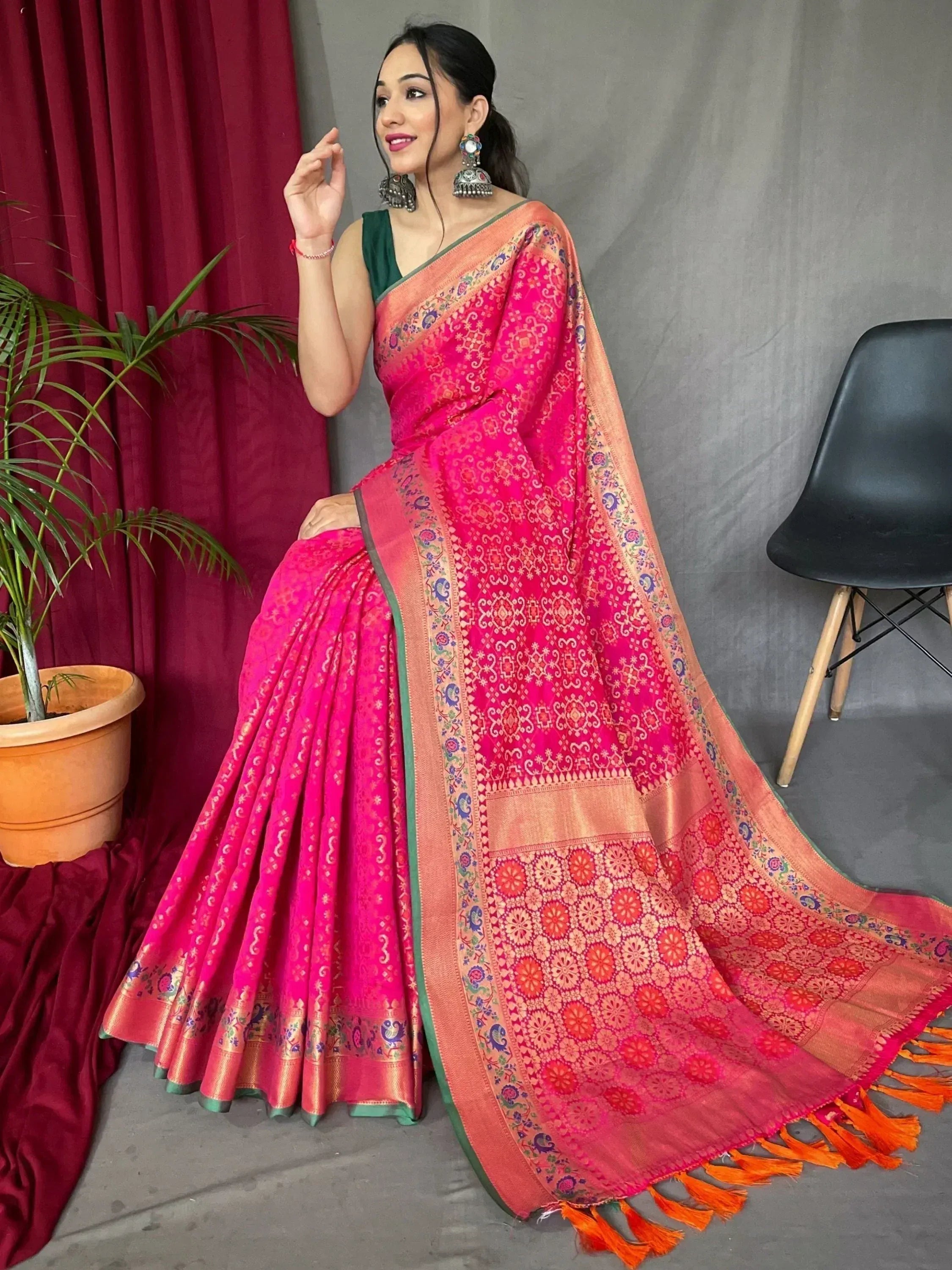 Vibrant pink ethnic saree with intricate floral patterns, gold border, and orange tassels, paired with green blouse.