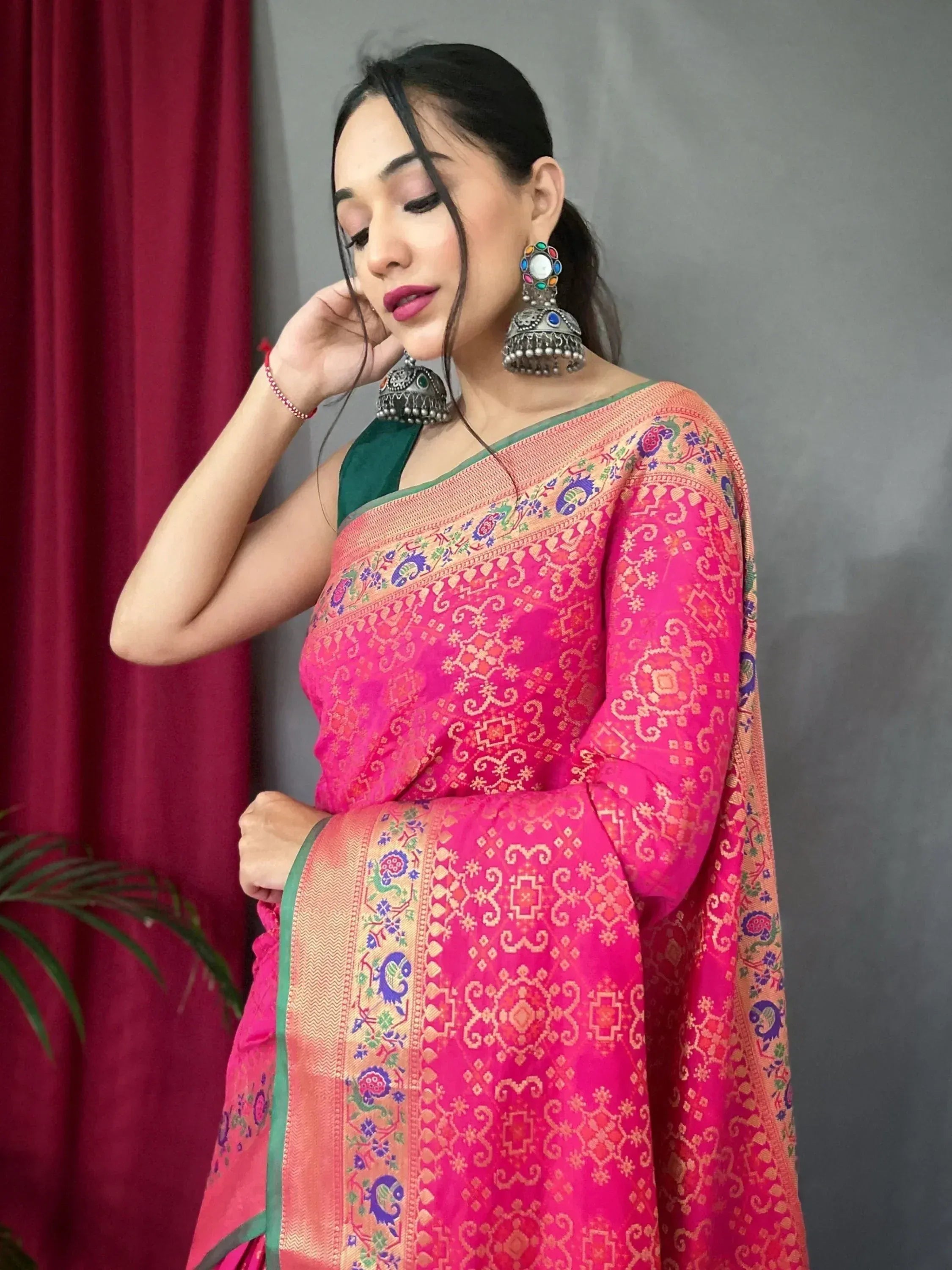 Woman in vibrant pink embroidered saree with green blouse, traditional Indian ethnic wear, paired with jhumka earrings